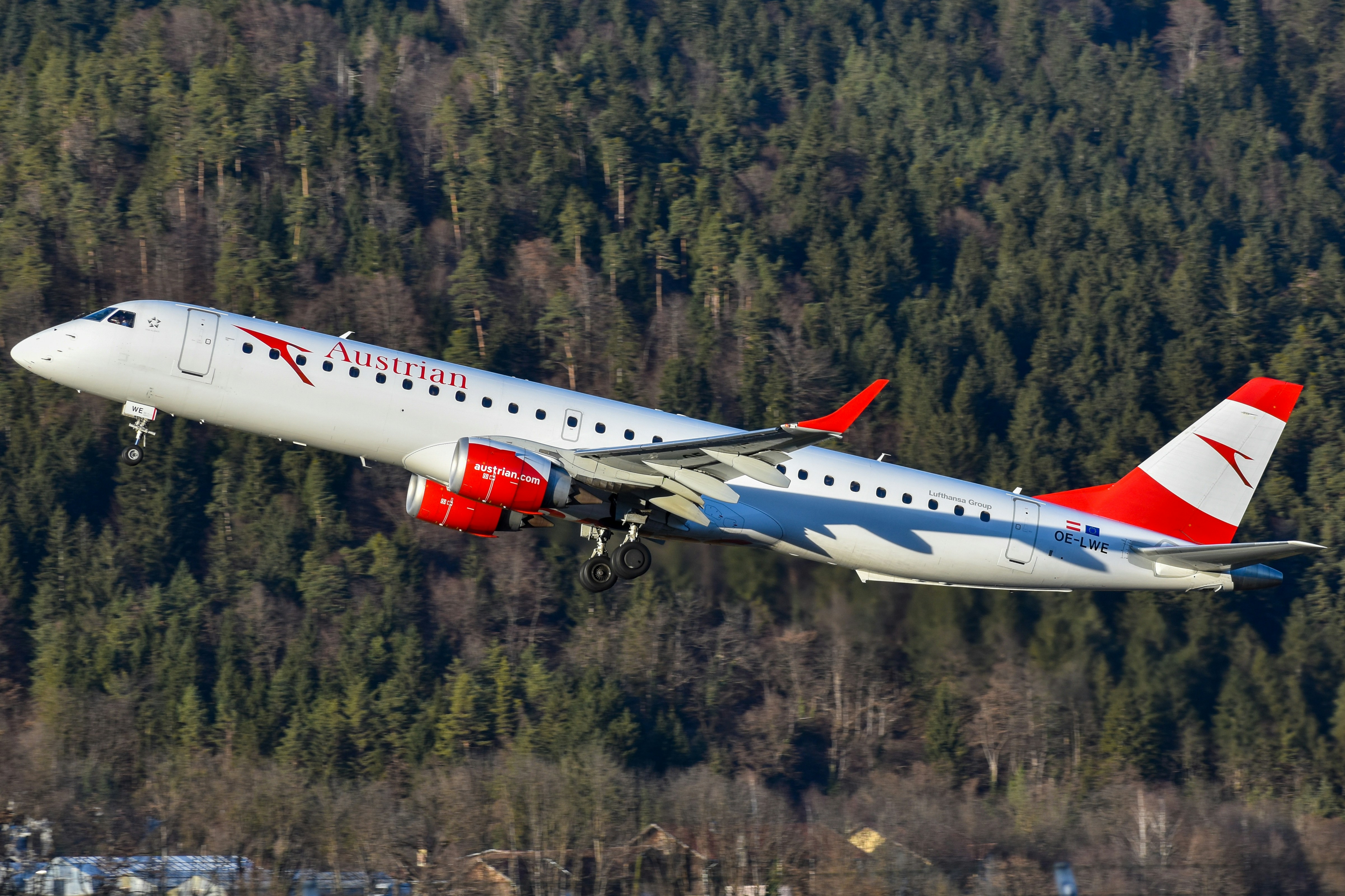 A large passenger jet flying over a forest, Austrian Airlines E195 departing Innsbruck