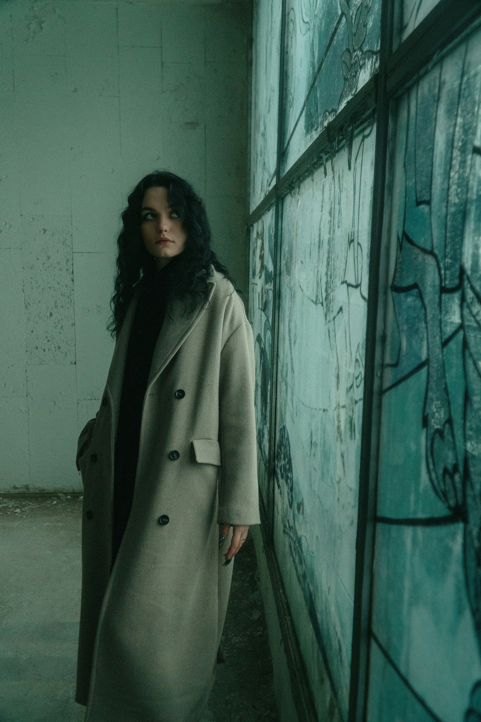 A woman in a long coat leaning against a wall