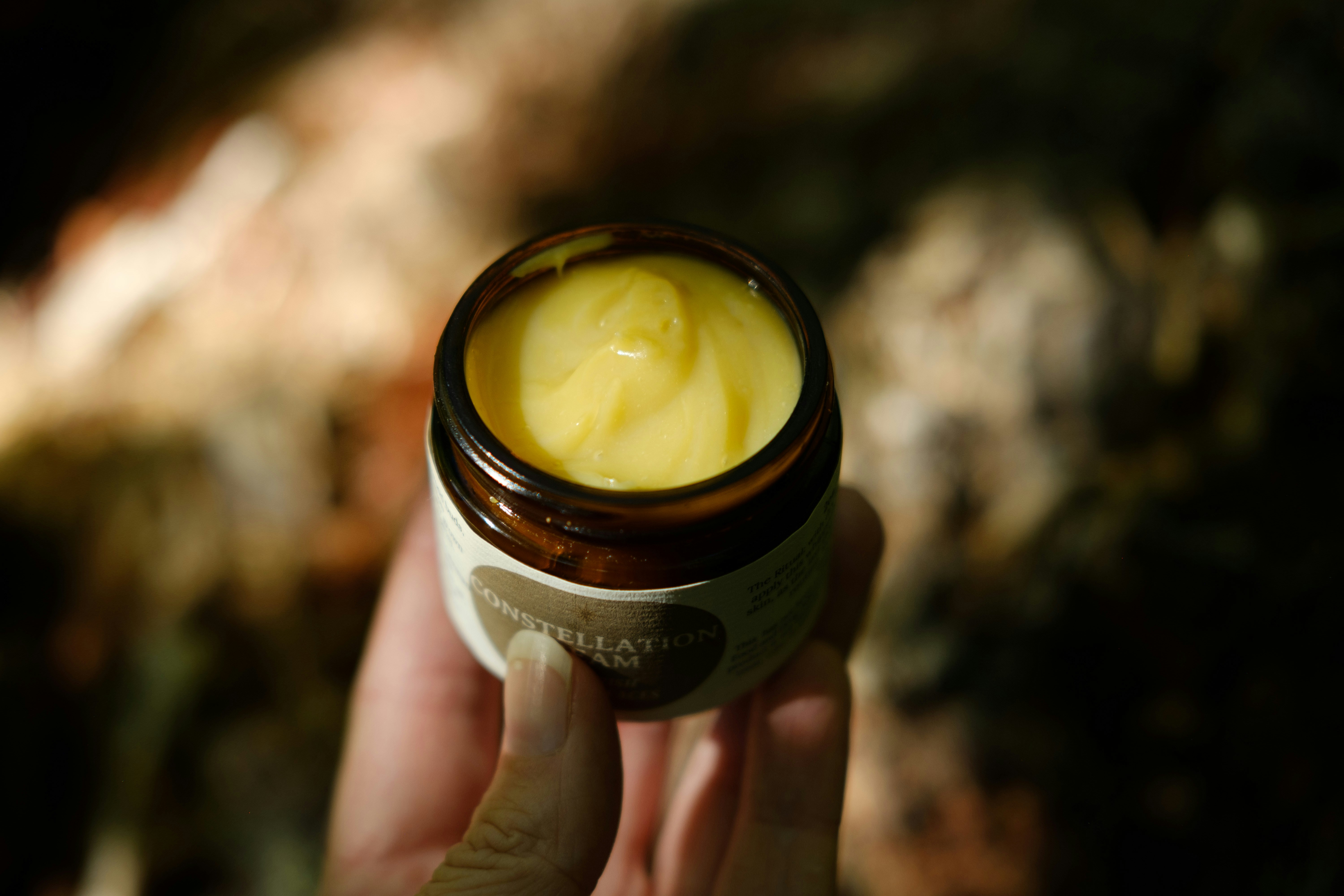 A hand holding a small jar of cream