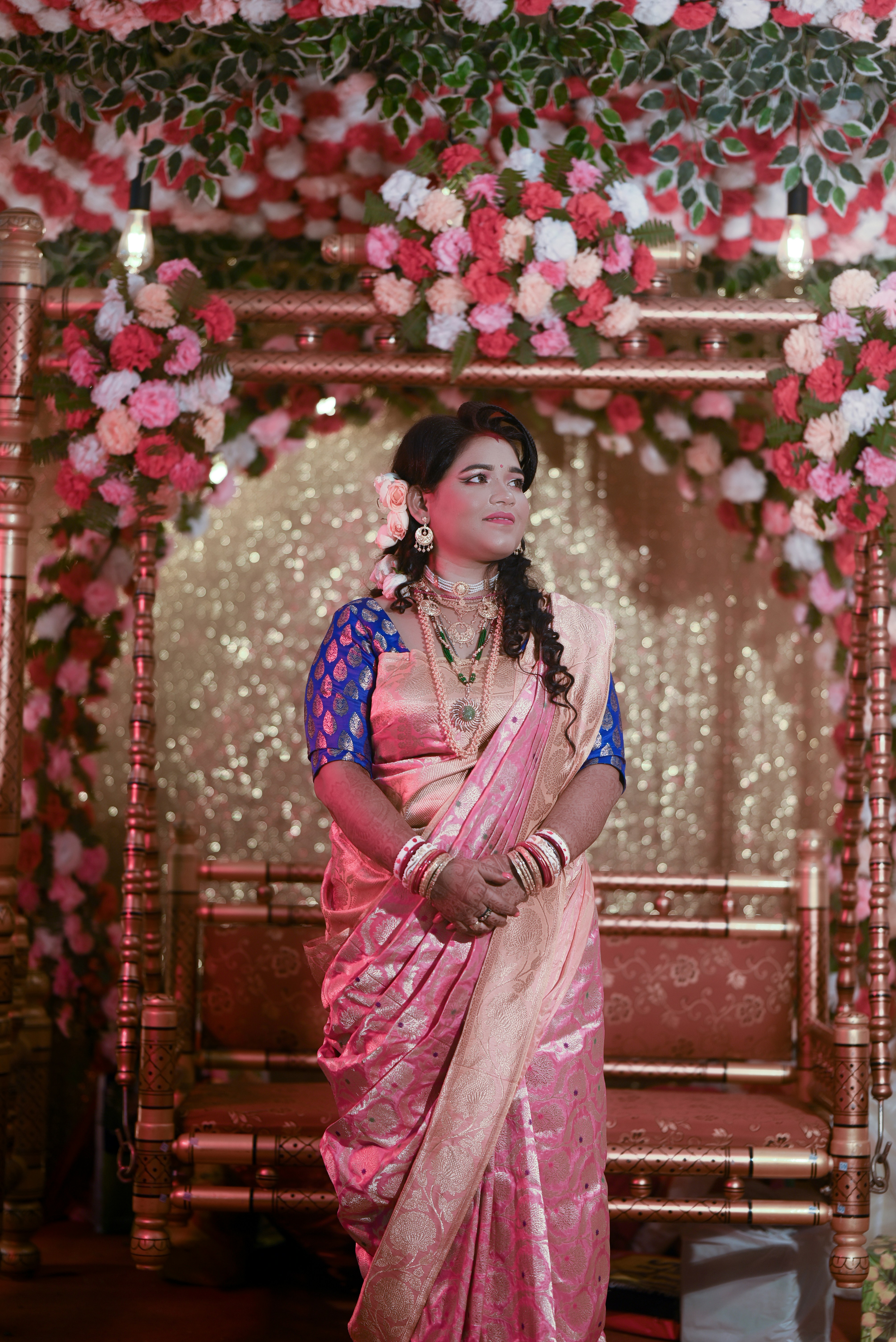 A woman in a pink sari standing under a floral arch