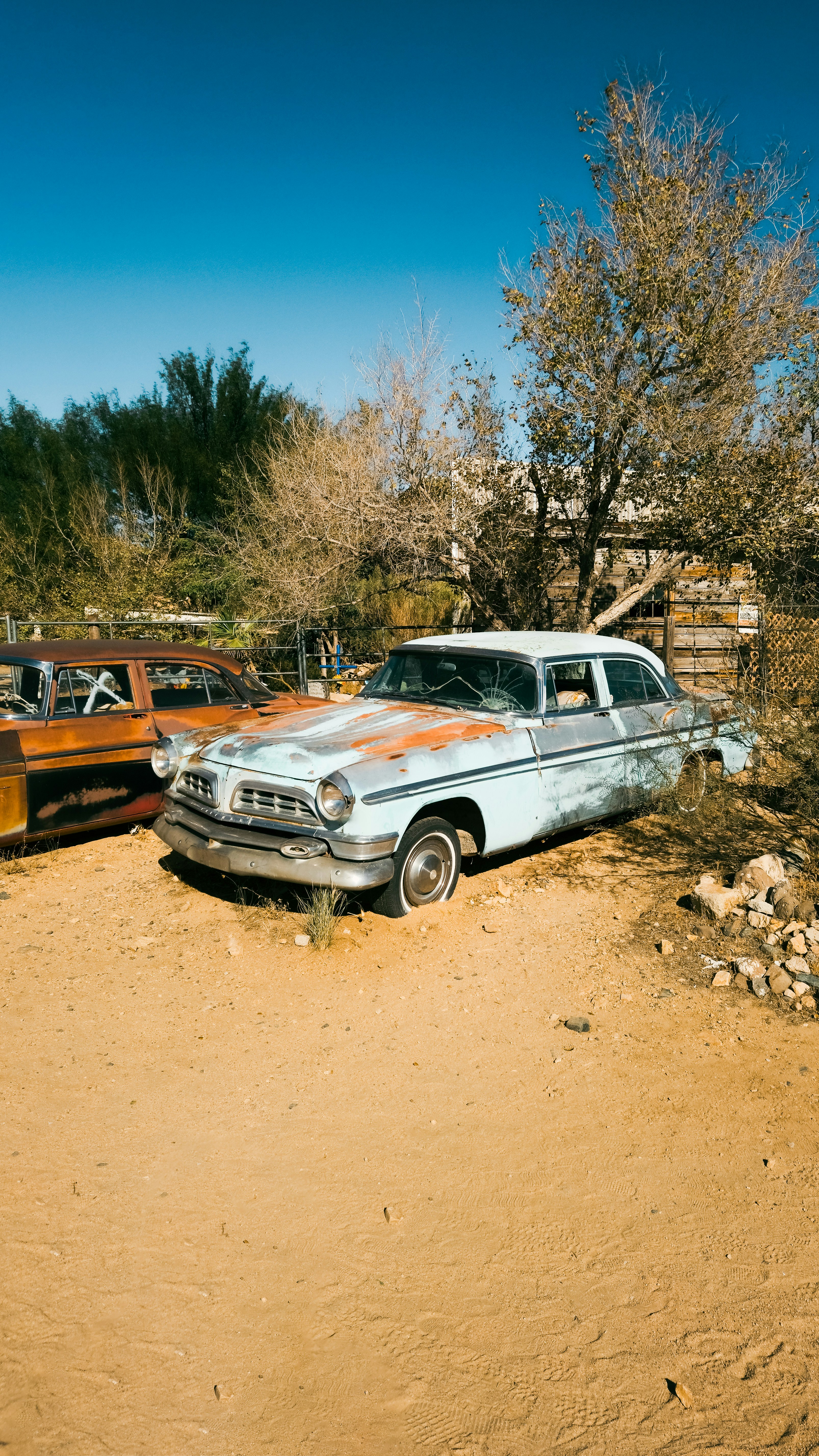 Two old cars are parked in the dirt