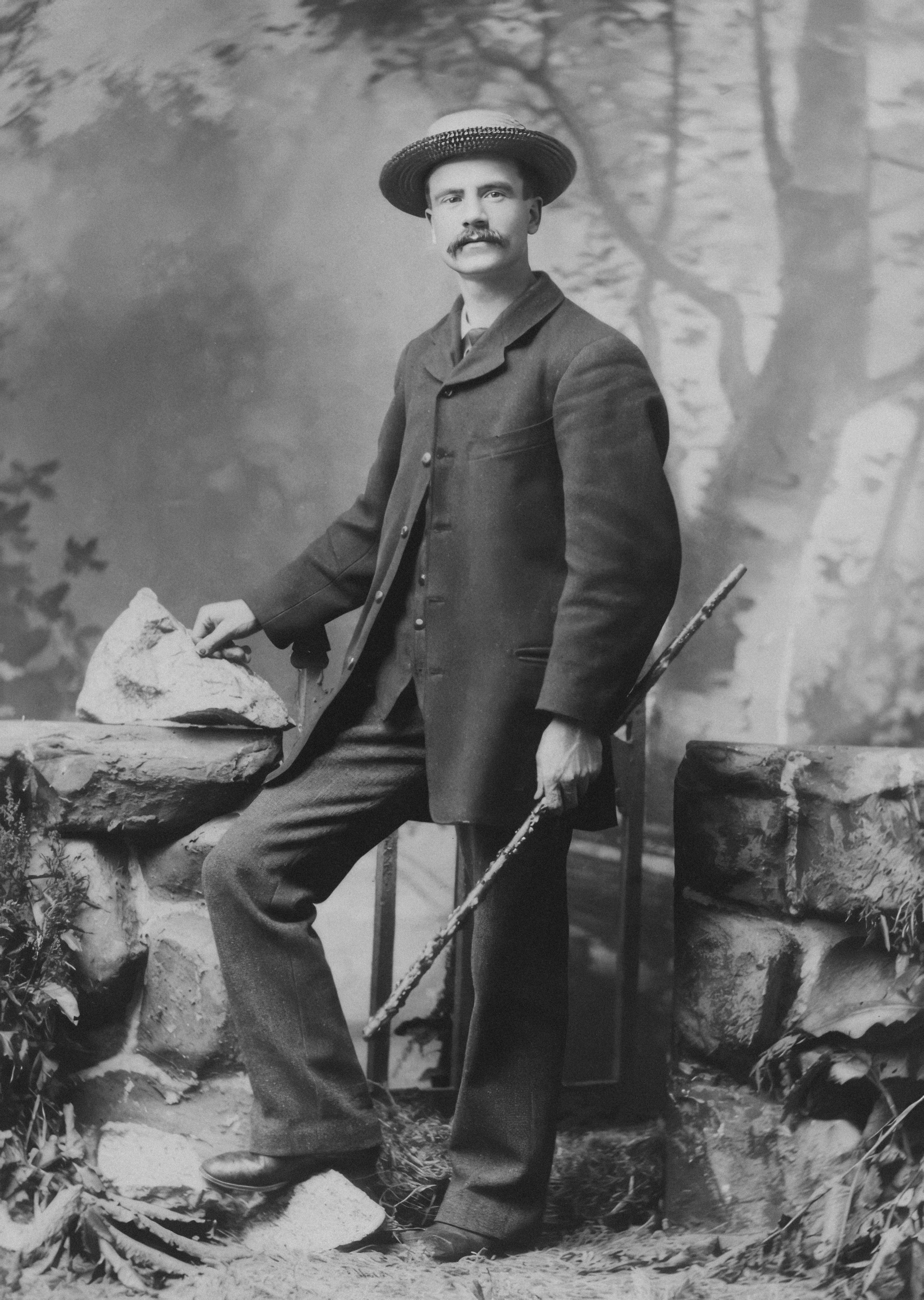 Man in suit and hat holding walking stick