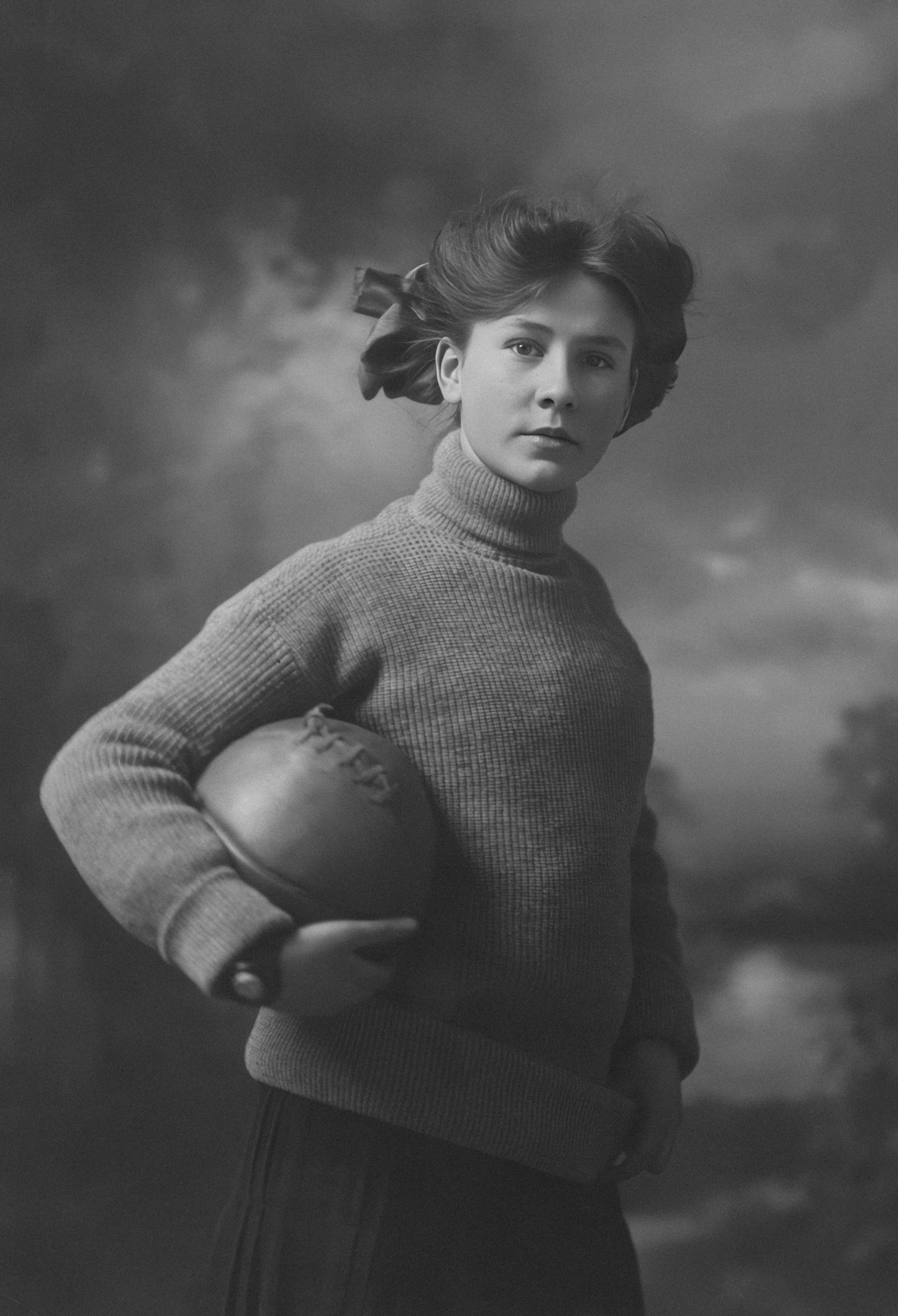 Young woman holding a ball against a cloudy background.