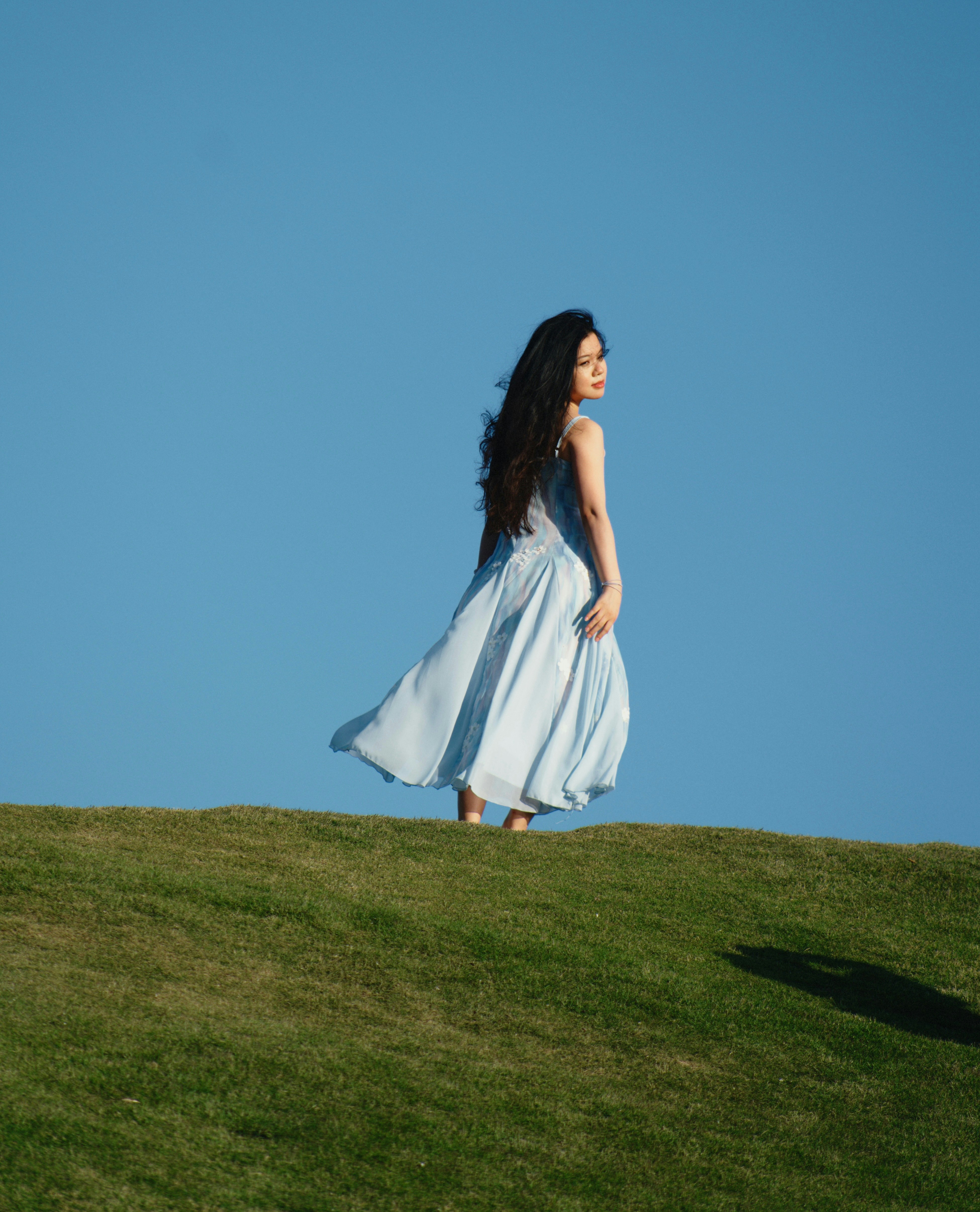 A woman in a white dress walking on a grassy hill