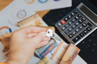 A person is putting money in front of a calculator