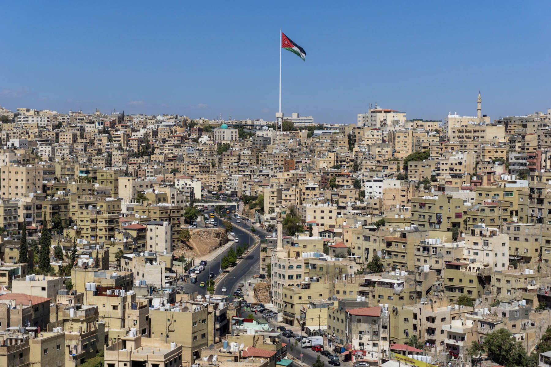 Amman's pale limestone neighbourhoods rising around a valley beneath the Jordanian flag