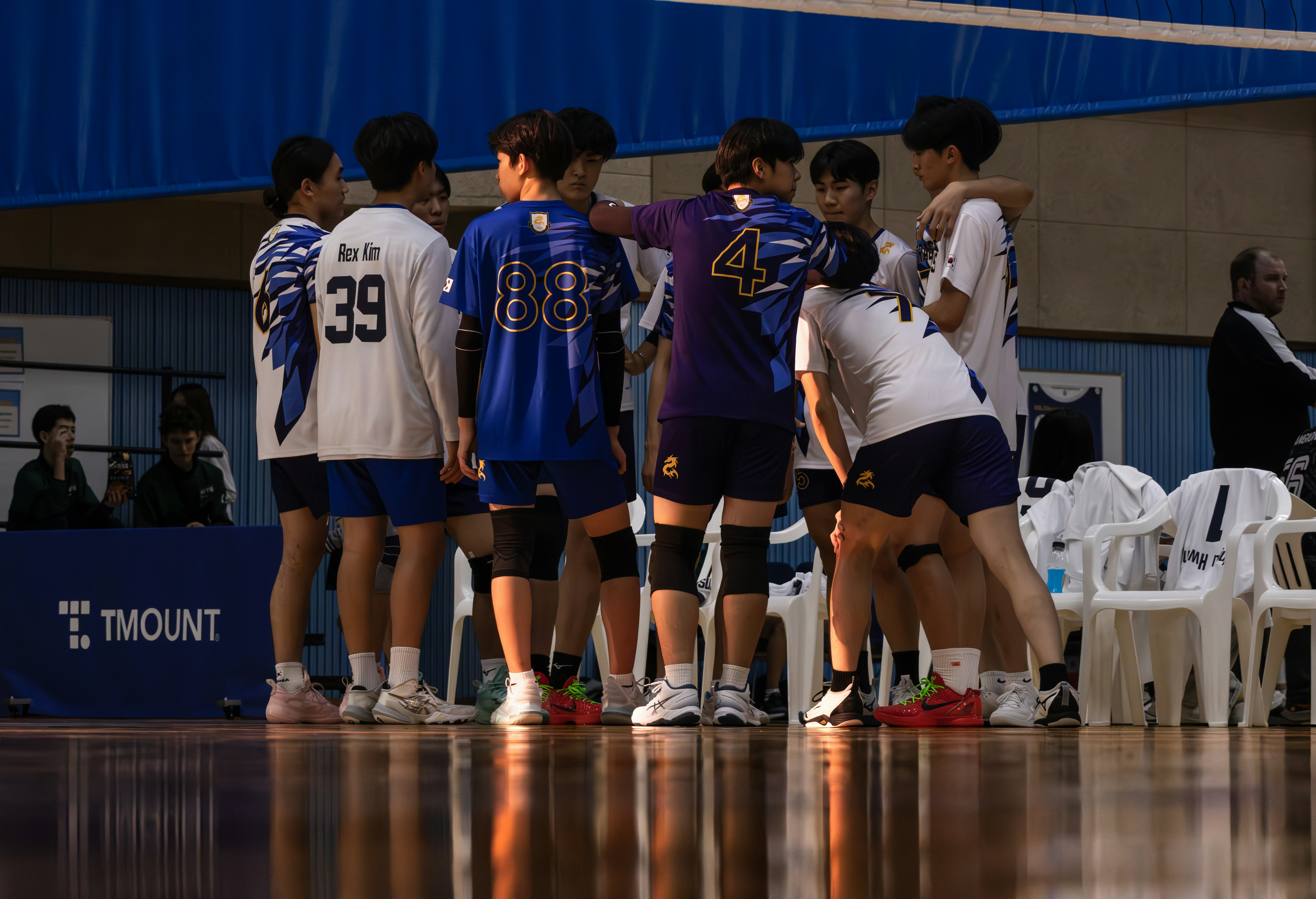 Volleyball team huddle on indoor court, bright overhead lights, athletic team in navy uniforms