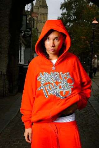 A man in an orange hoodie standing on a sidewalk