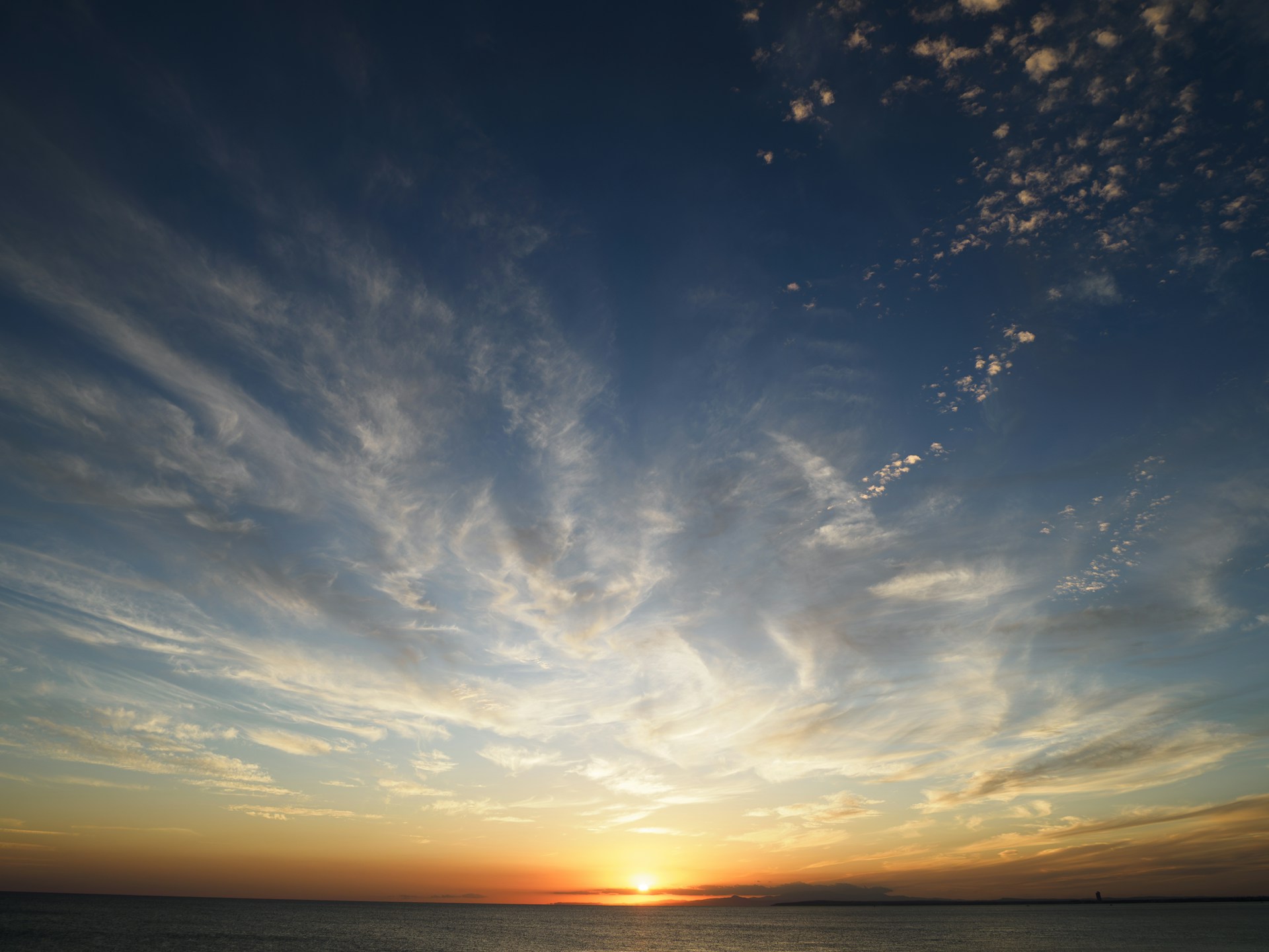 The sun is setting over the ocean with clouds in the sky