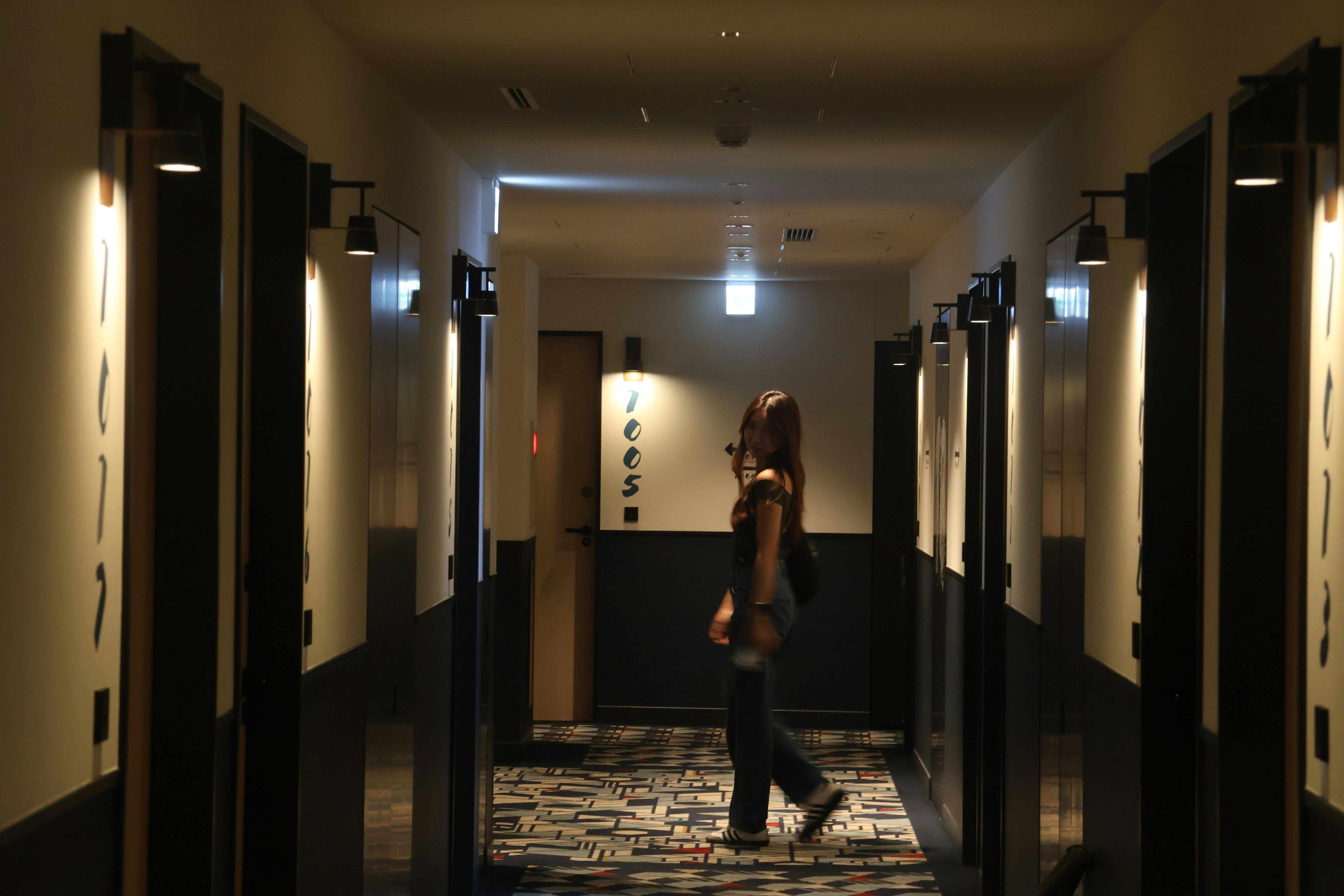 A dimly lit hotel corridor with numbered doors, one door (313) slightly open as a cold blue light spills through the crack.