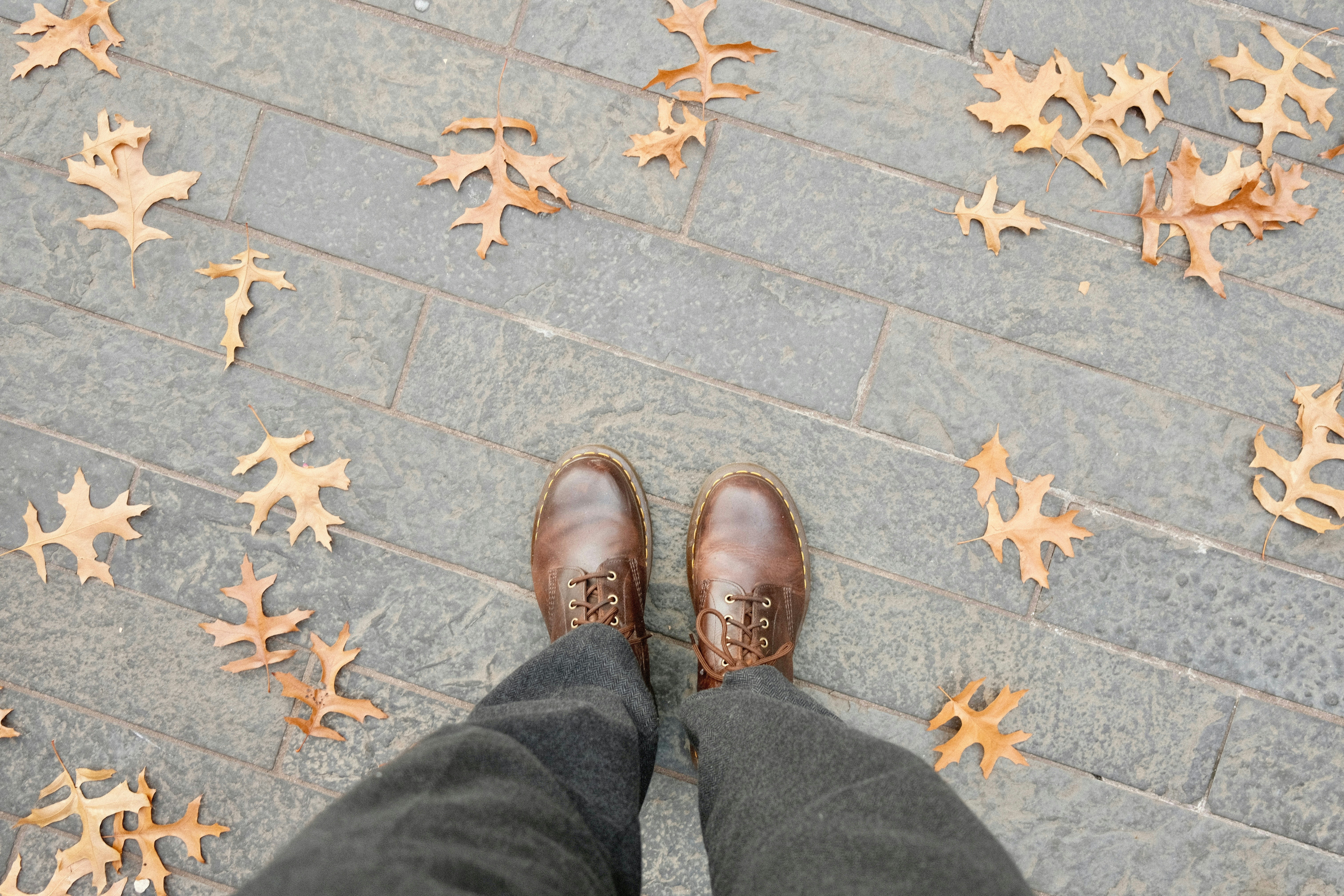A person standing on a sidewalk with brown shoes