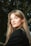 A woman with long blonde hair standing in front of a tree