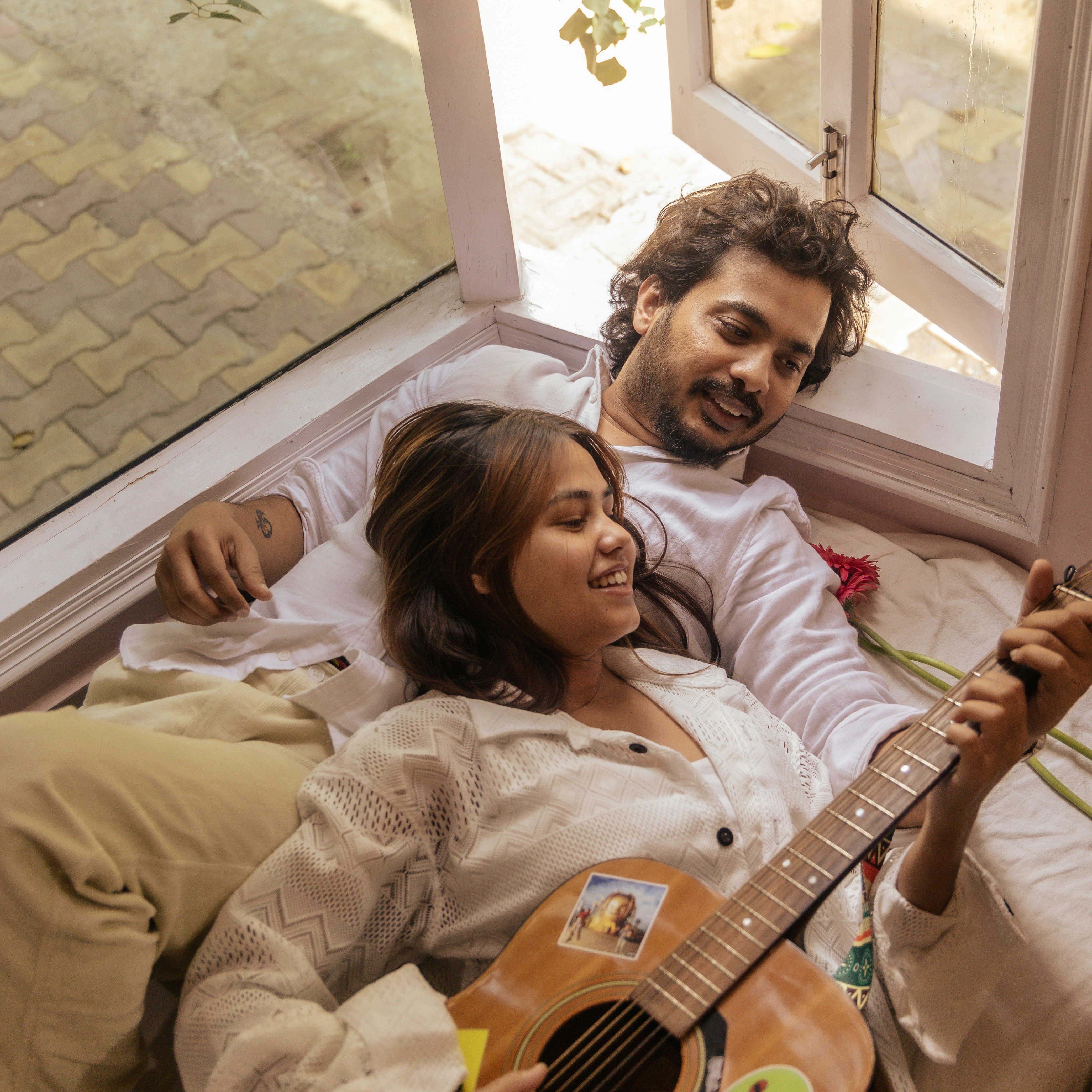 A man and a woman laying on a bed with a guitar