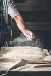 A person in an apron sprinkling flour on a table