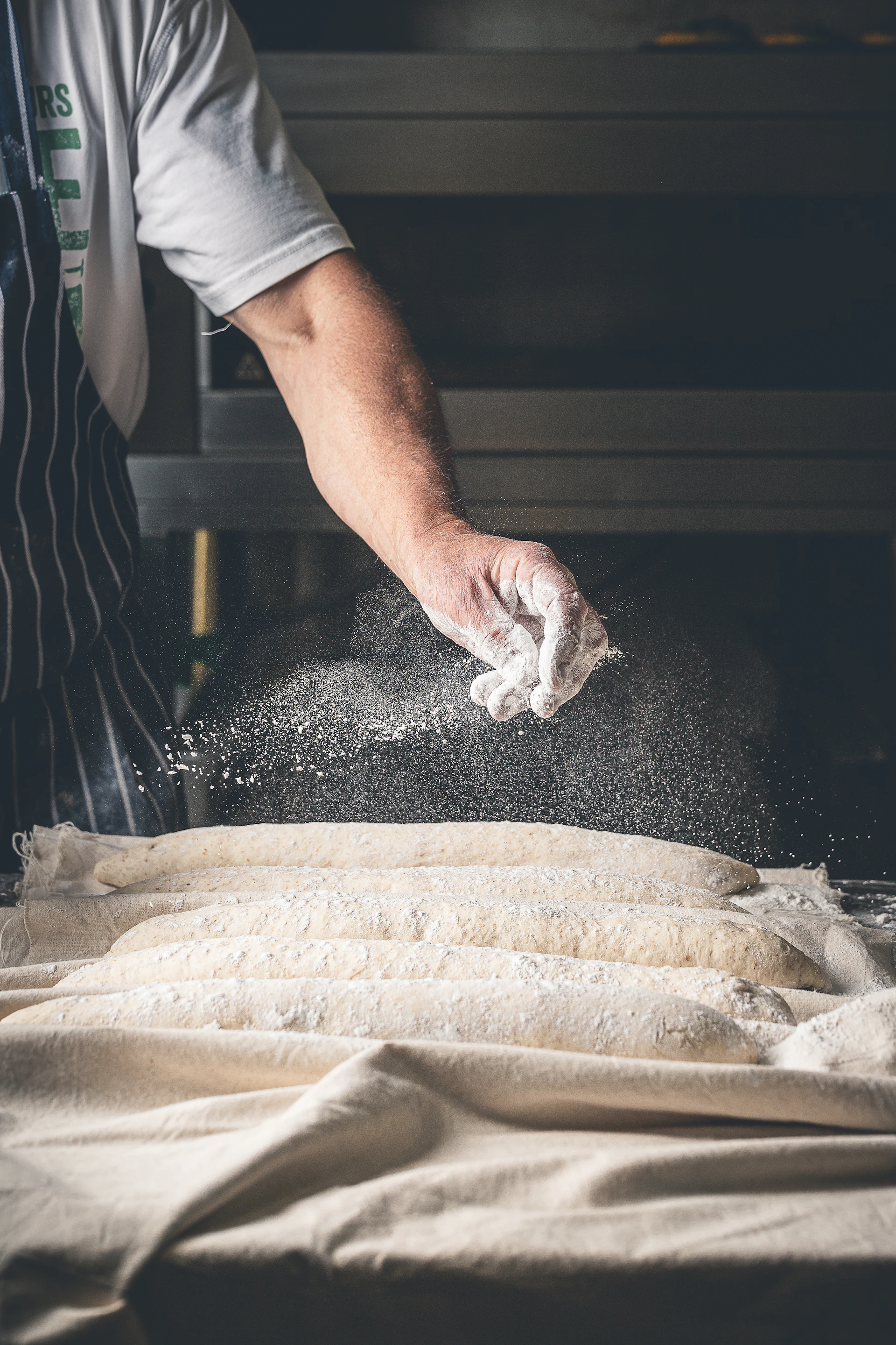 A person in an apron sprinkling flour on a table