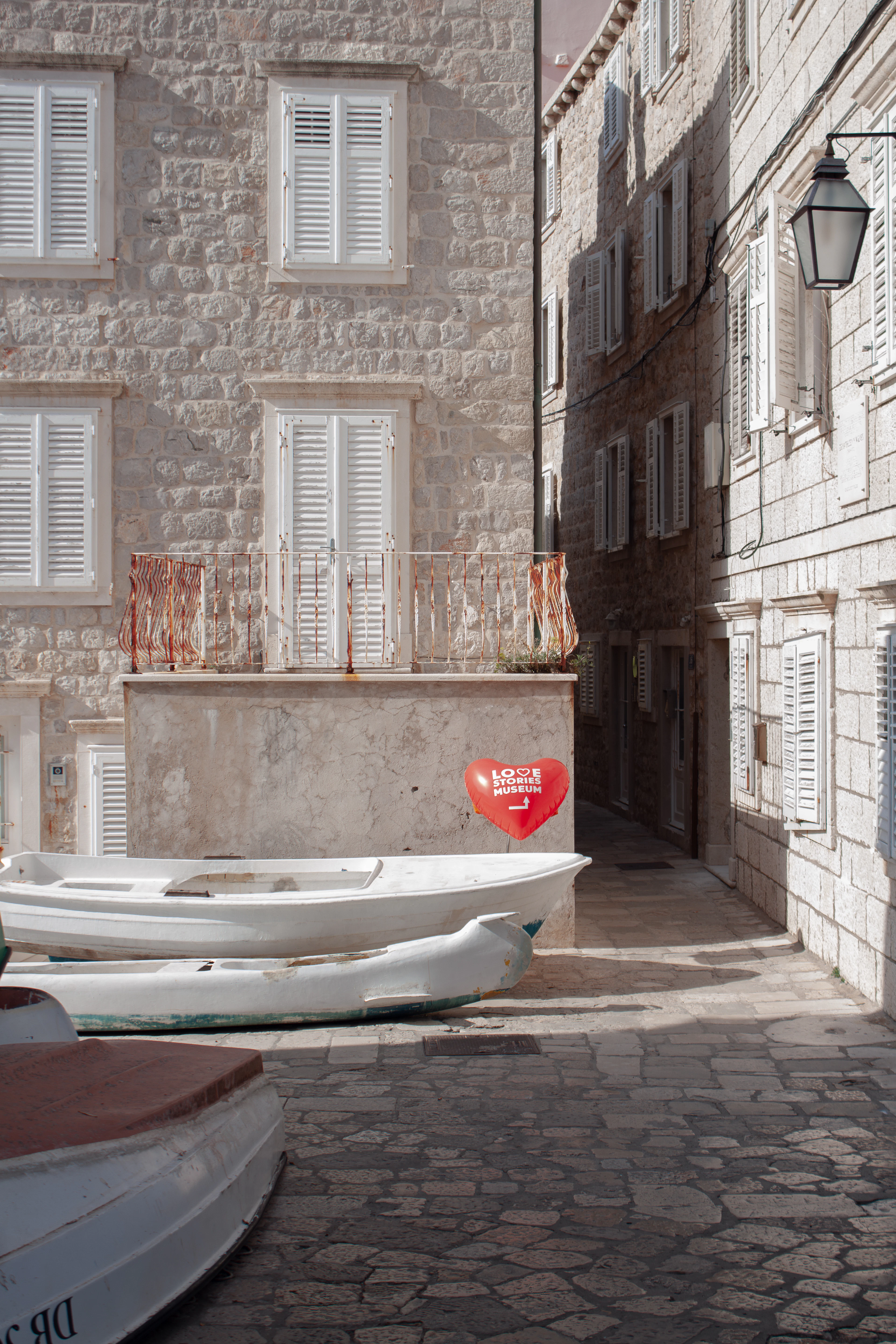 A quiet limestone alley in Dubrovnik's Old Town, small white boats propped on the flagstones beneath shuttered windows and a wrought-iron lantern.