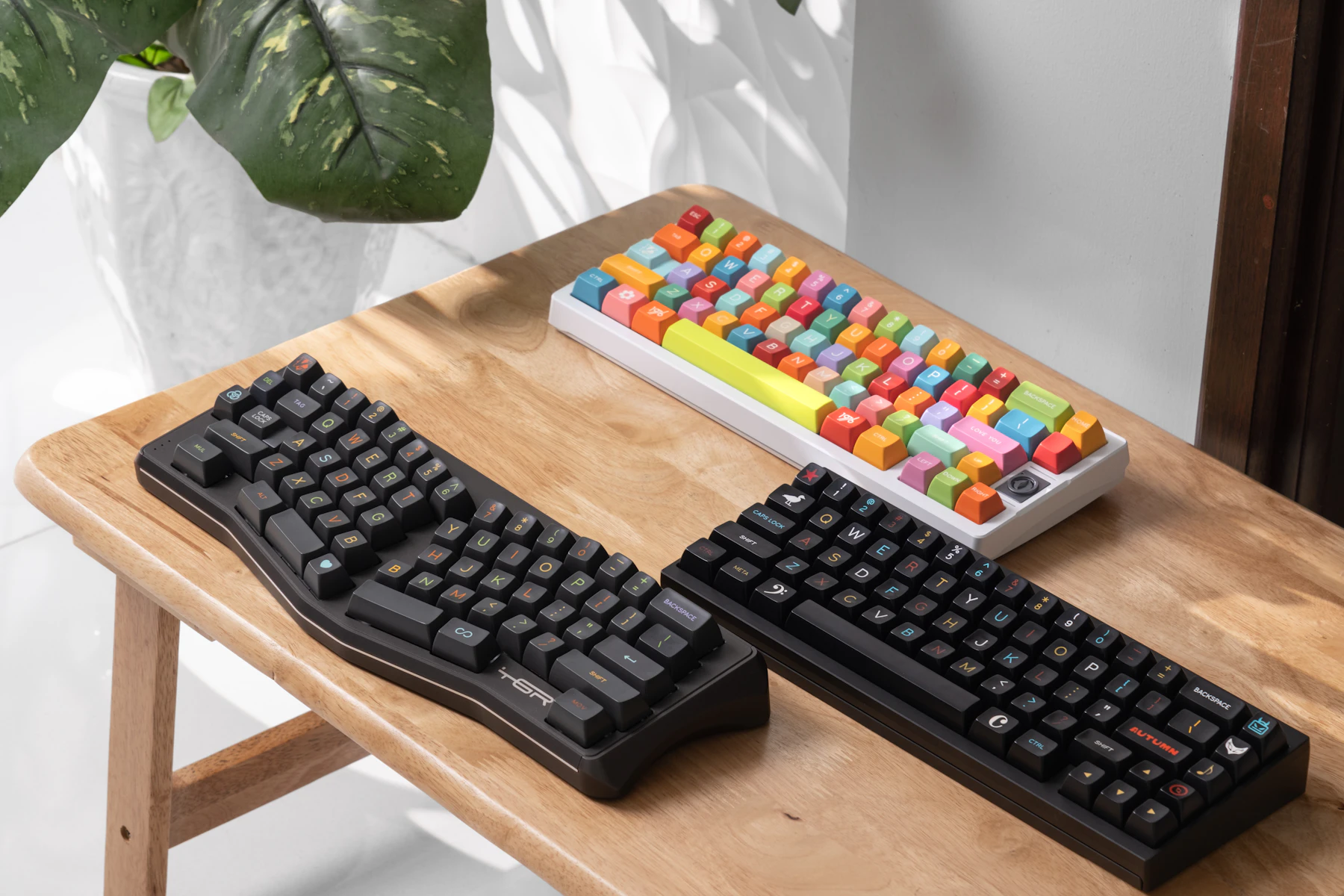 Three mechanical keyboards lying side by side on a wooden table
