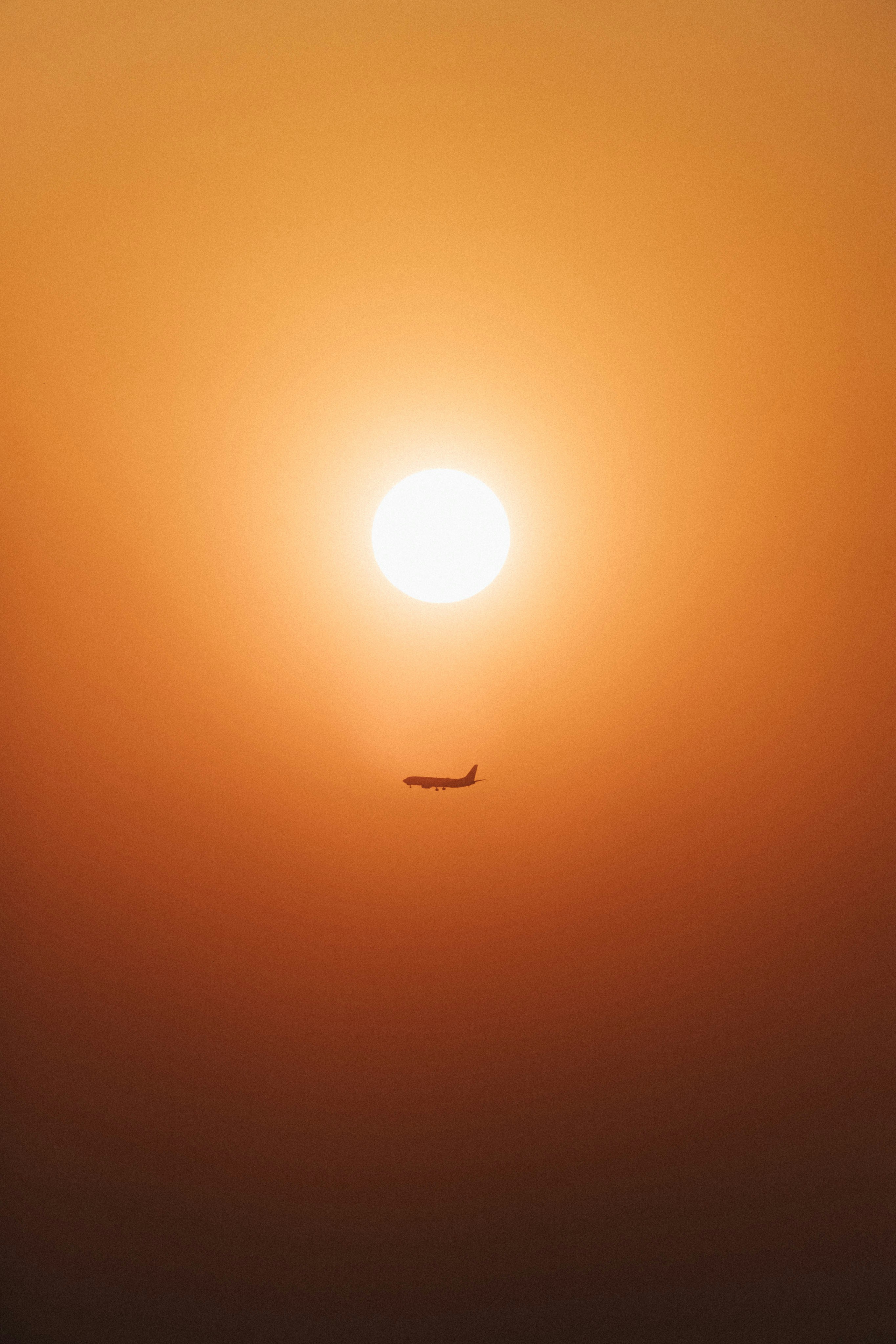A plane flying in the sky with the sun in the background