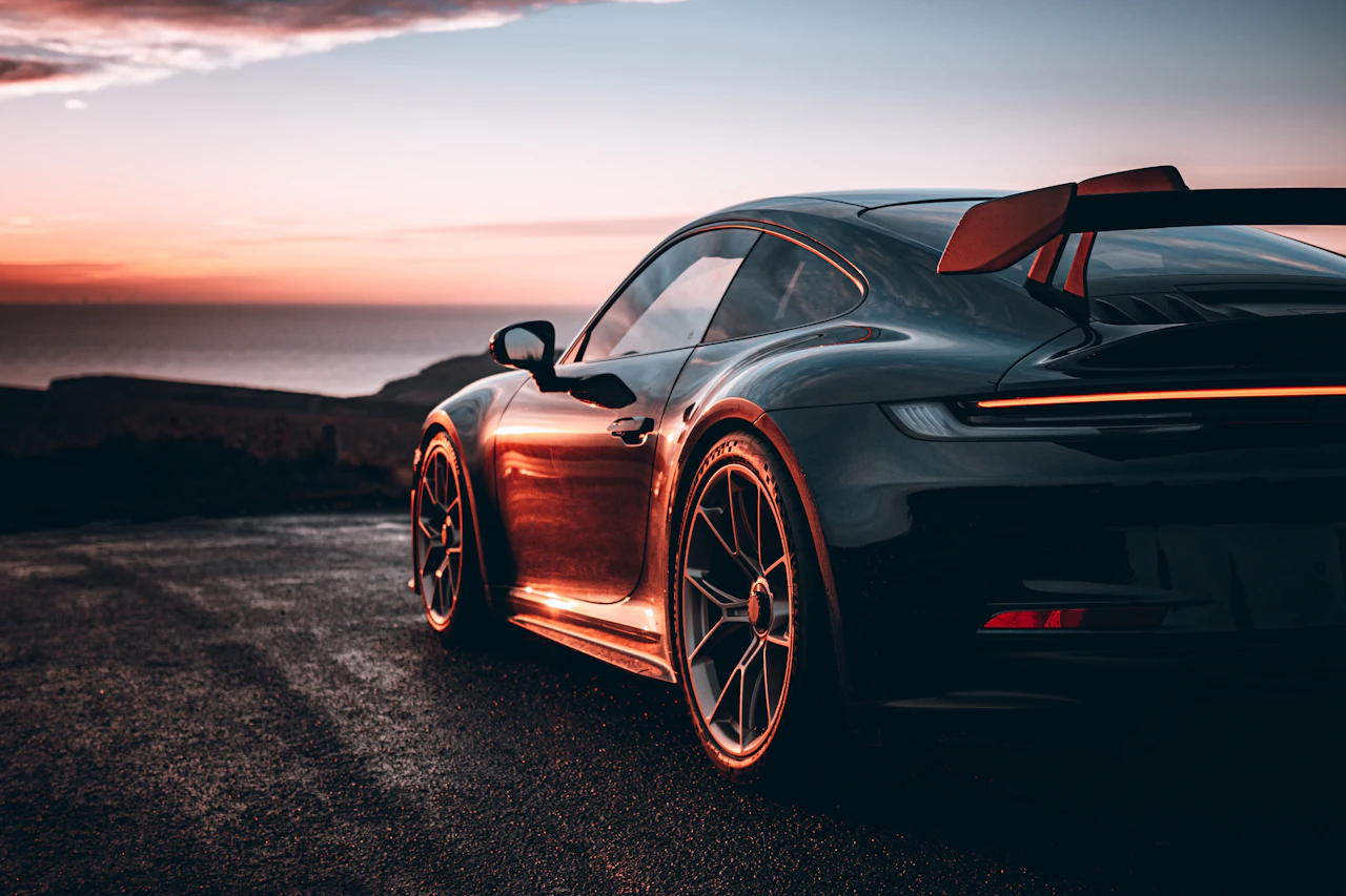 Porsche 911 GT3 noire vue de trois quarts arrière, aileron déployé, au coucher du soleil