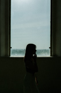 A woman standing in front of a window talking on a cell phone