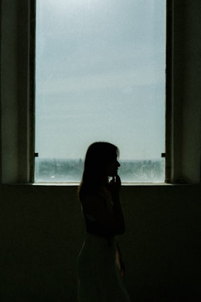 A woman standing in front of a window talking on a cell phone