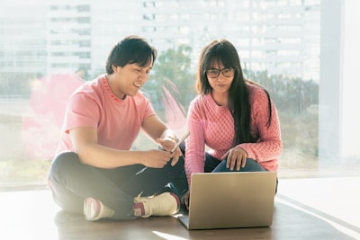 A man and a woman sitting on the floor with a laptop