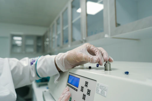 A person in a lab coat and gloves working on a machine