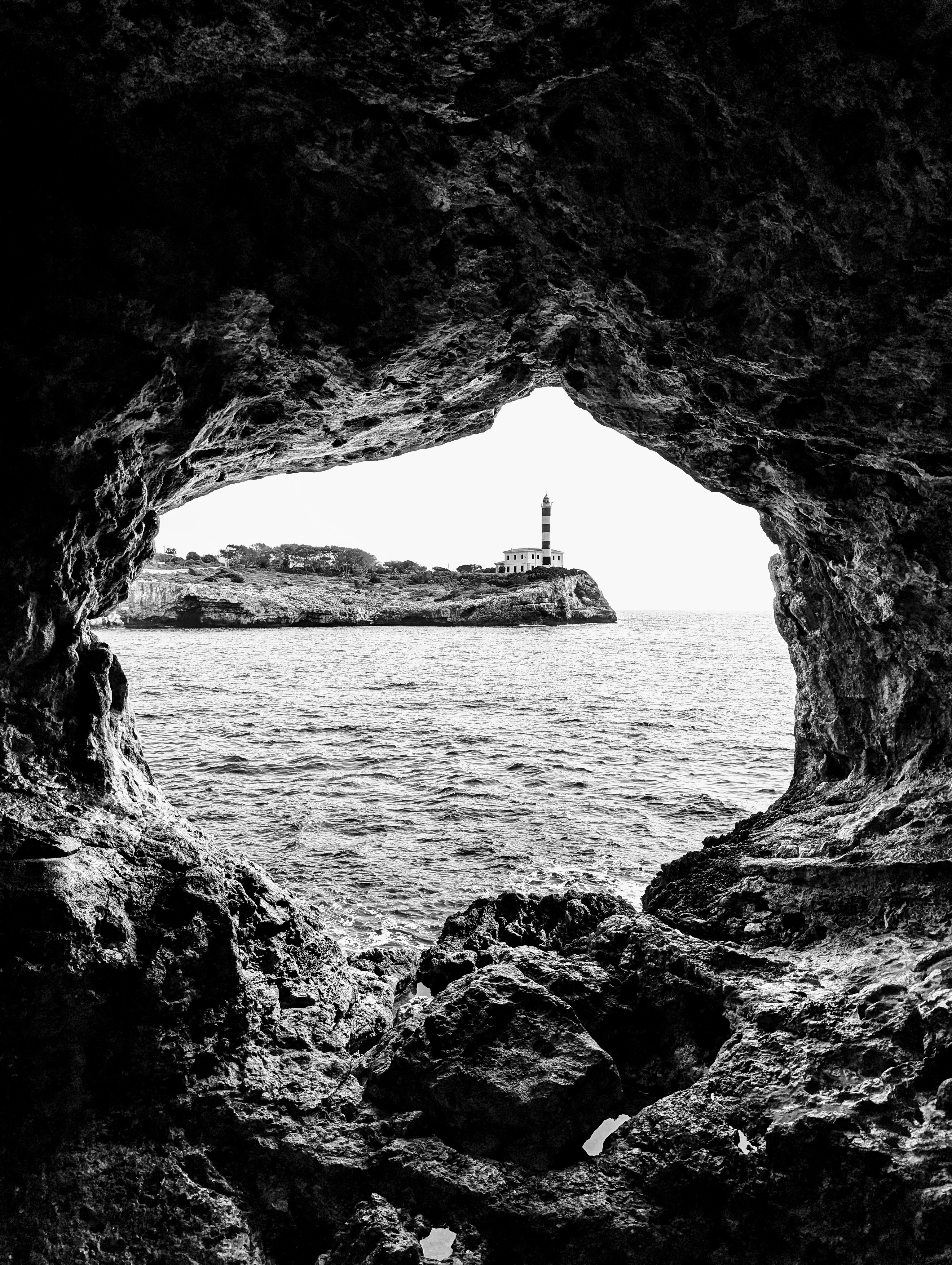 A black and white photo of a lighthouse through a cave