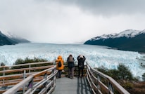 A group of people standing on a bridge looking at a glacier