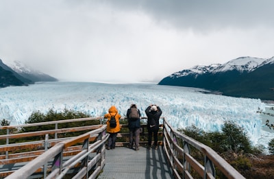 A group of people standing on a bridge looking at a glacier
