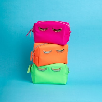 A stack of three colorful bags with eyelashes on them