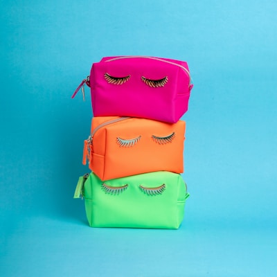 A stack of three colorful bags with eyelashes on them