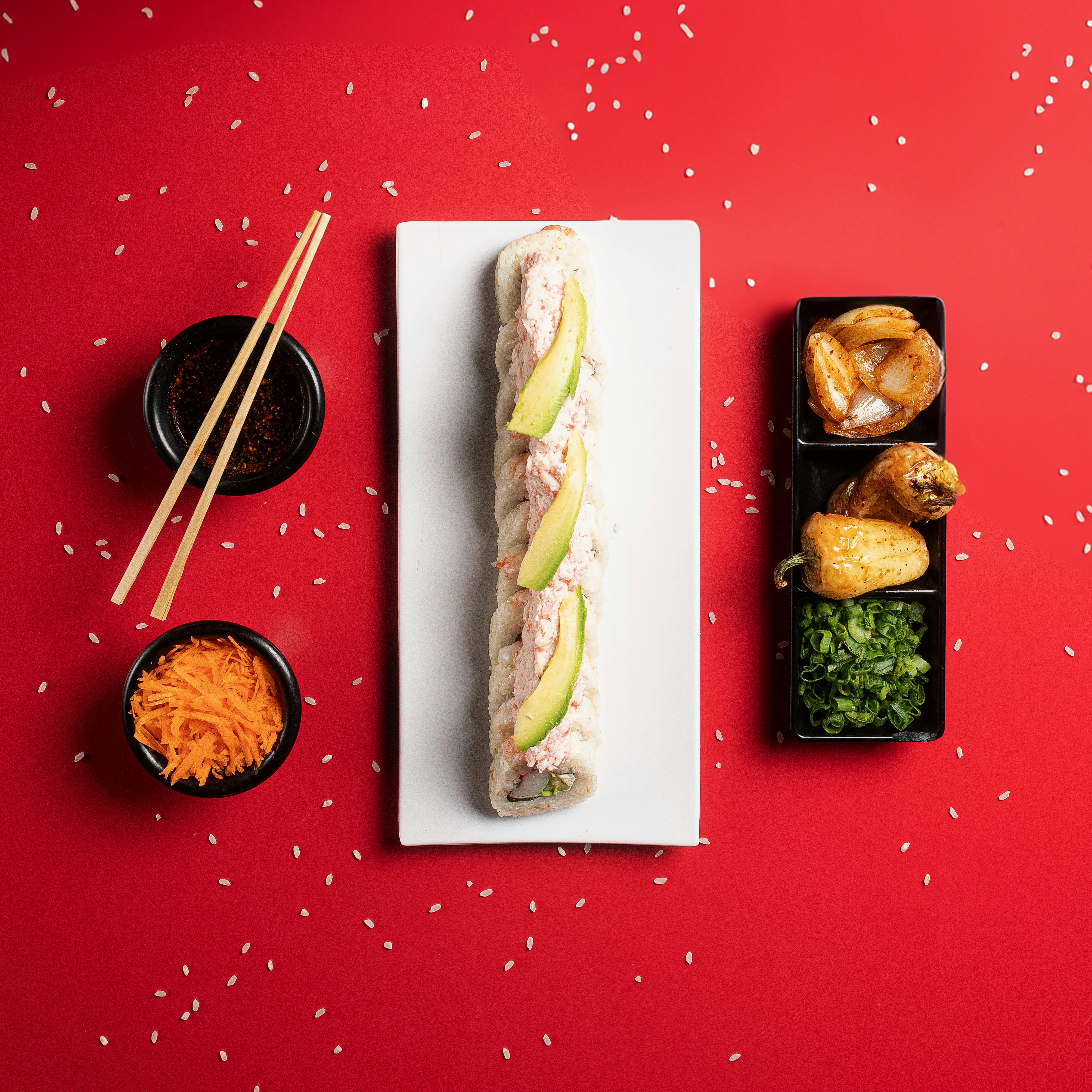 A sushi roll is on a plate with chopsticks and a bowl of