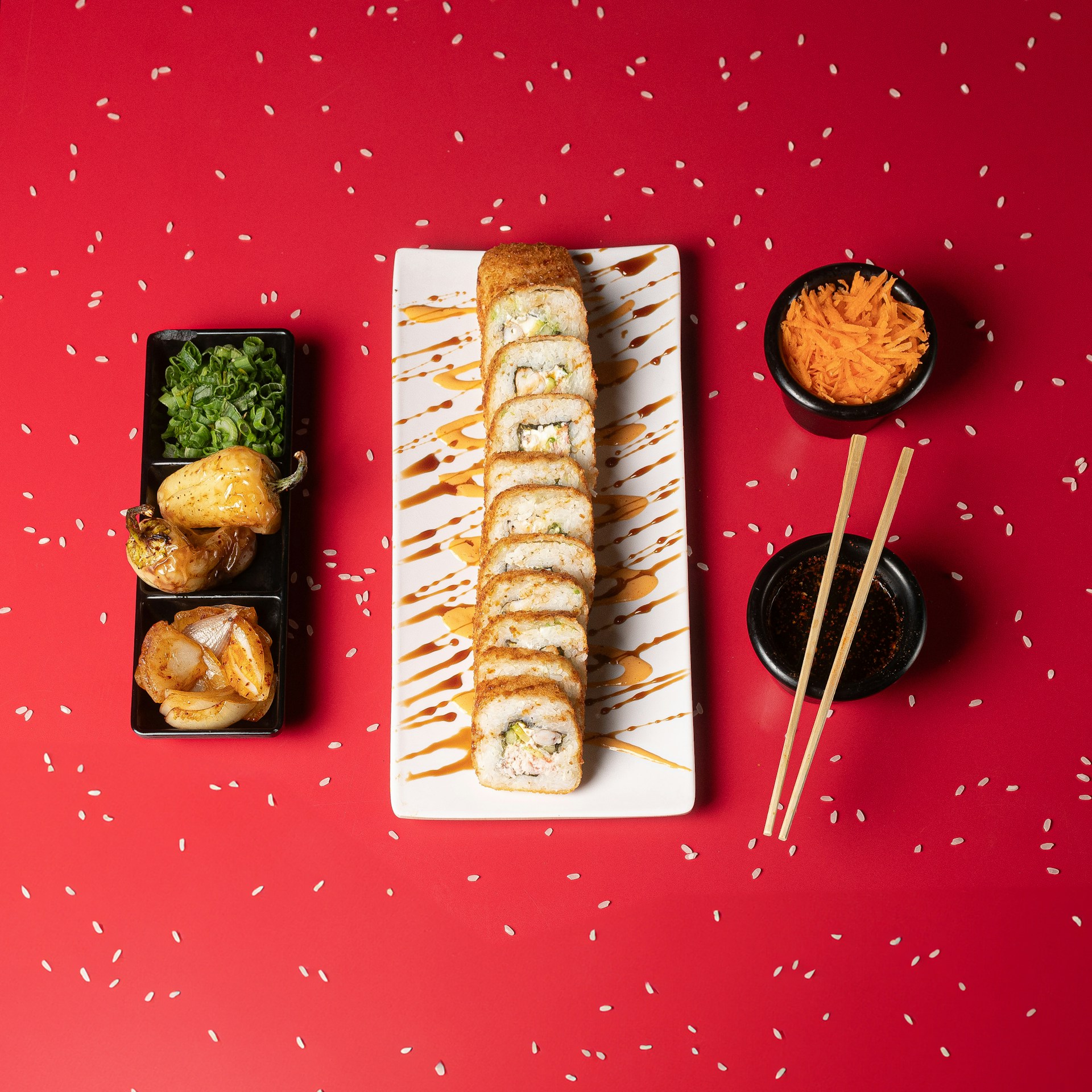 A red table topped with sushi and chopsticks