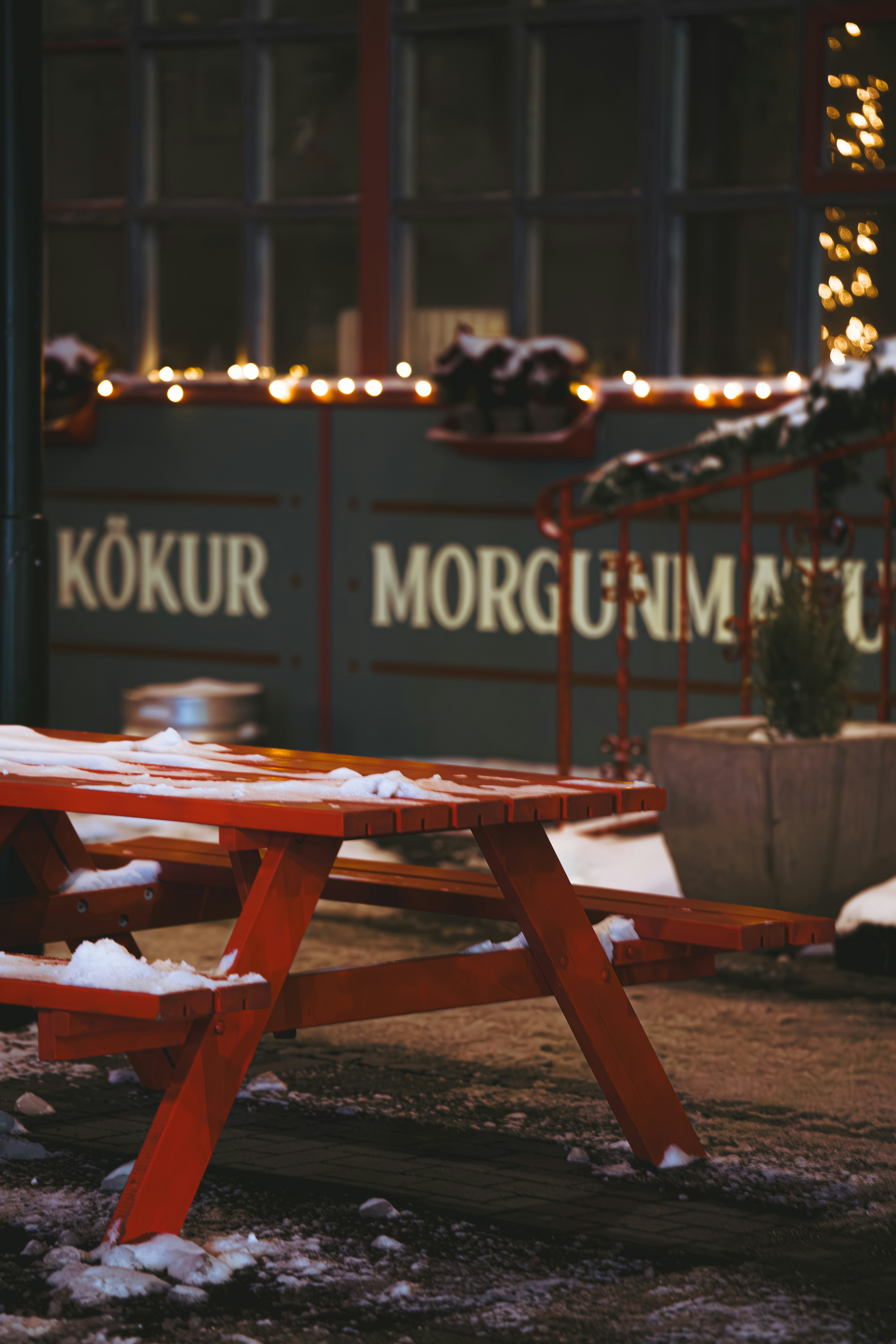 A red picnic table covered in snow in front of a building