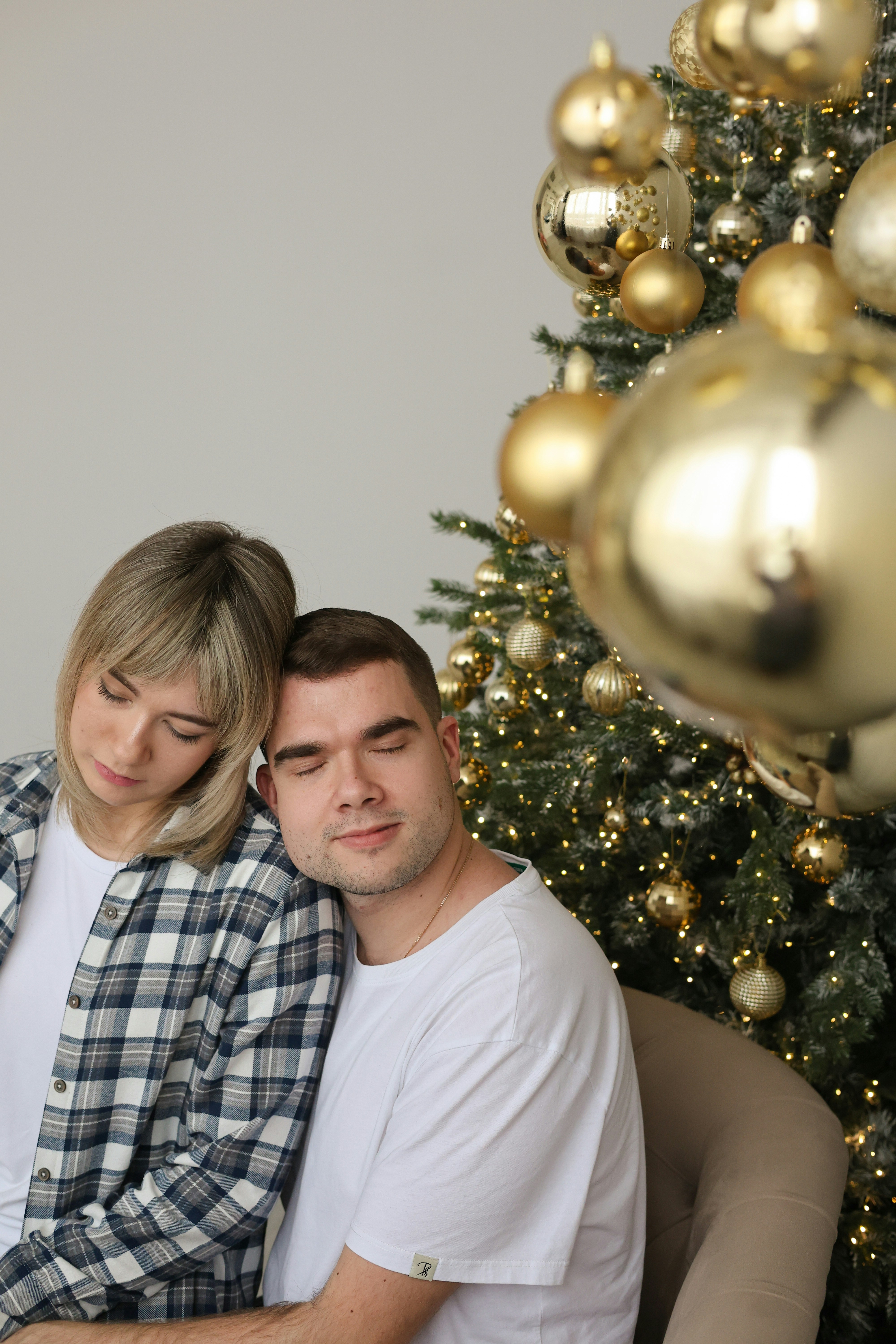 A man and woman sitting next to a christmas tree