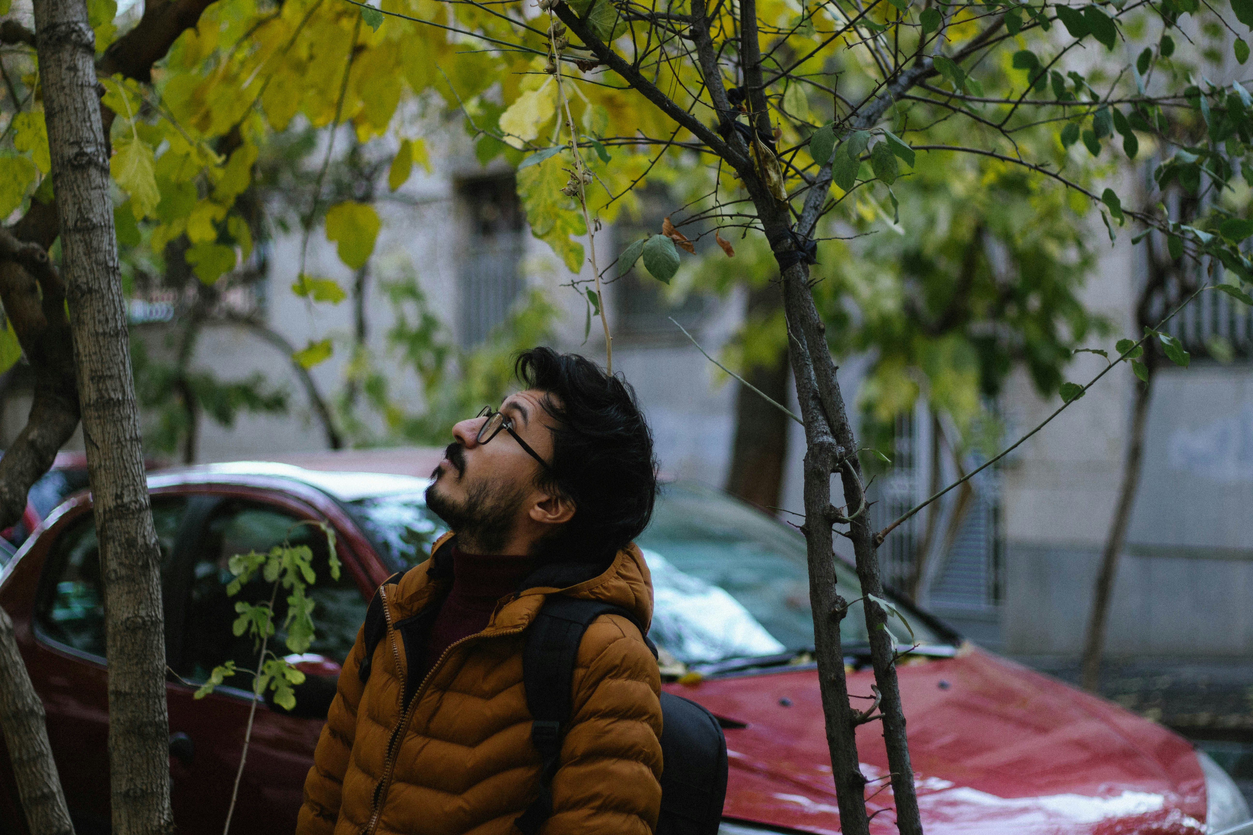 Un uomo in piedi accanto a un albero con un'auto rossa sullo sfondo