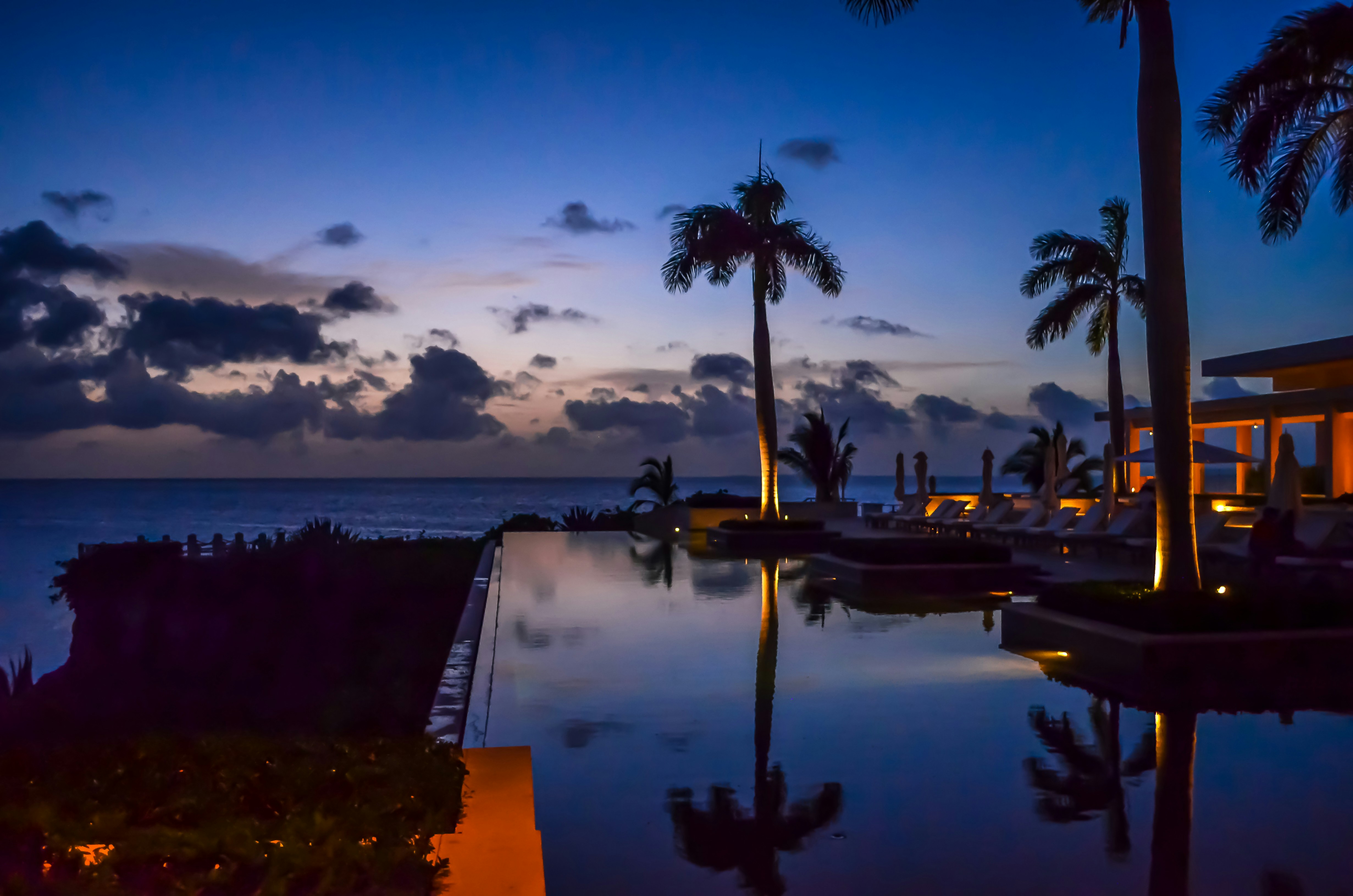 Luxury villa with infinity pool and city lights view at dusk, warm ambient lighting, dark tropical sky