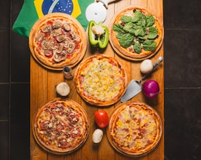 A table topped with four pizzas next to a flag