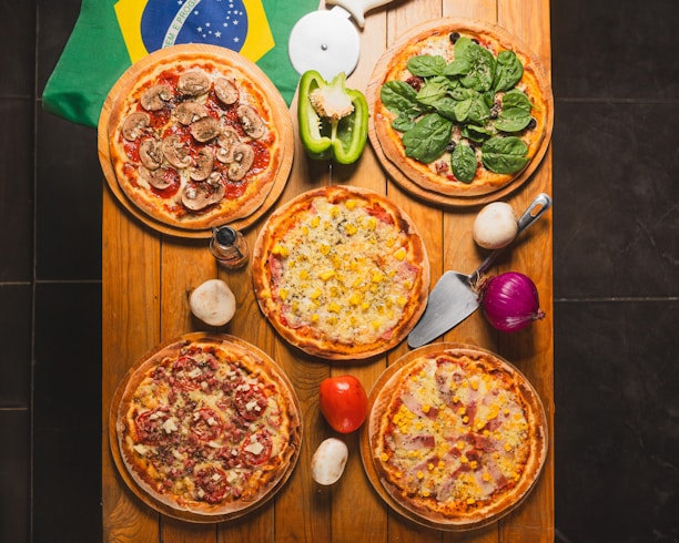 A table topped with four pizzas next to a flag