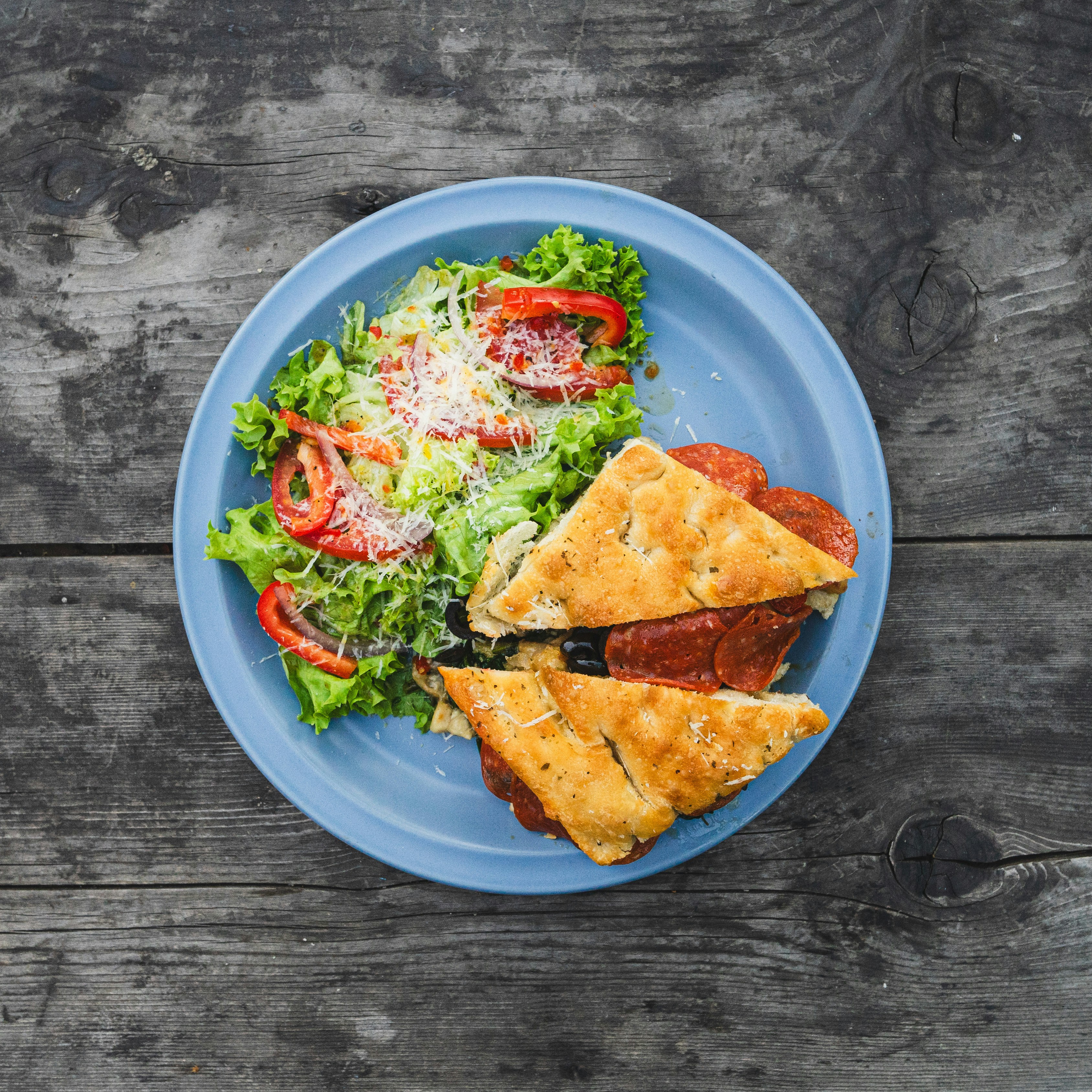 Un plato azul cubierto con una ensalada y dos rebanadas de pizza