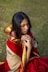 A woman in a red and gold sari sitting on the ground