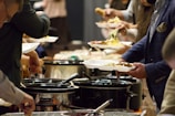 A group of people standing around a buffet line