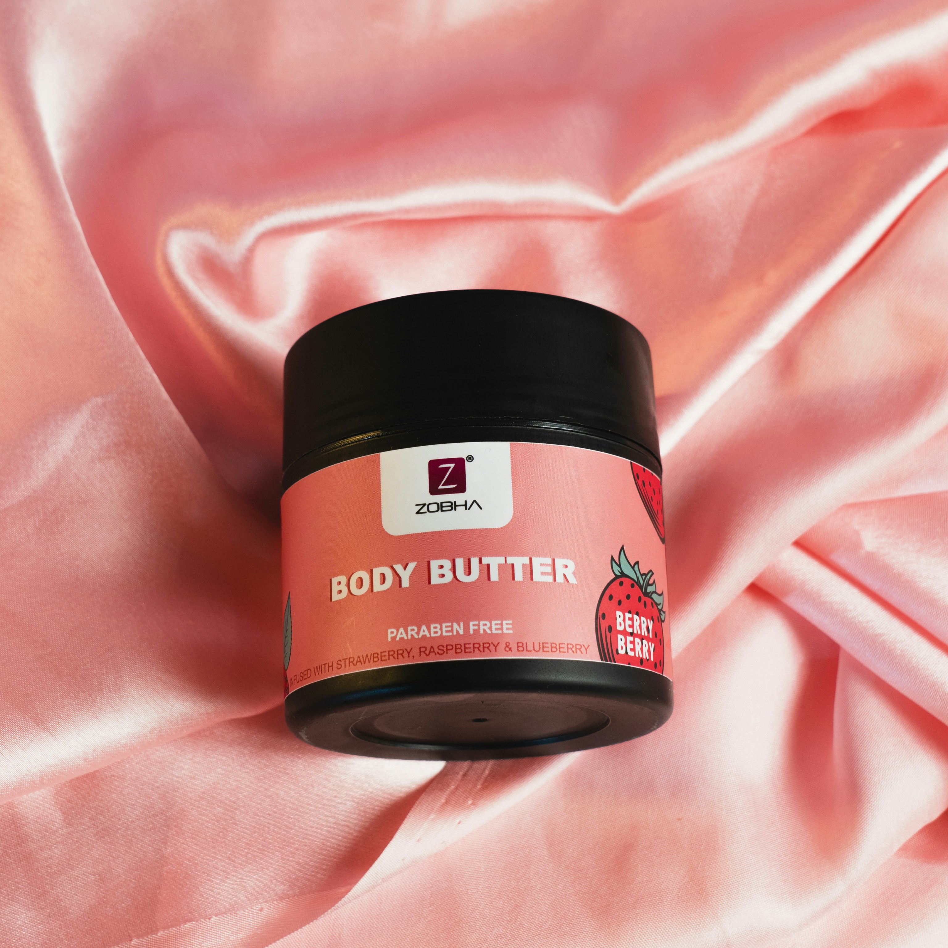 A jar of body butter sitting on a pink satin
