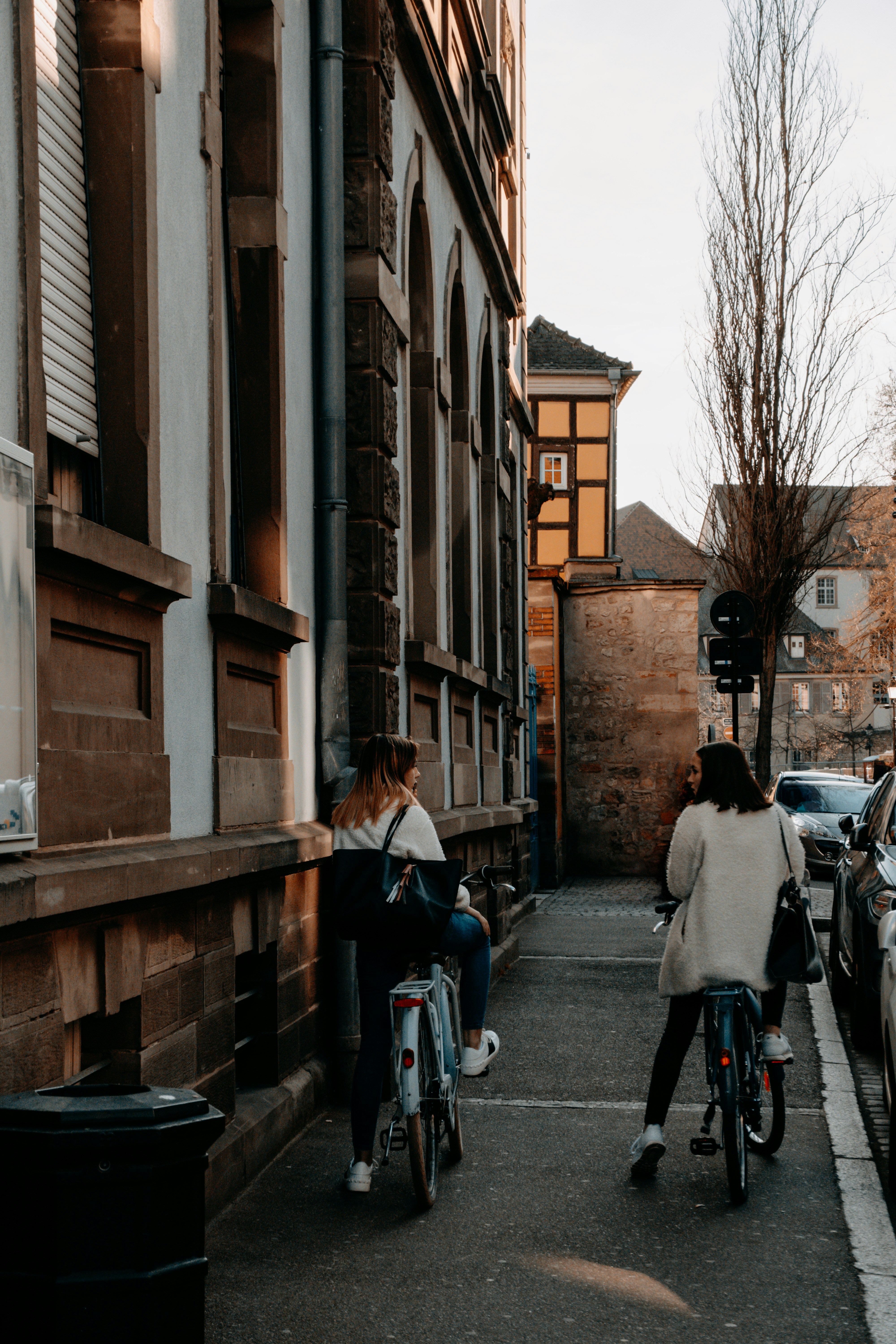 A woman riding a bike down a street next to parked cars