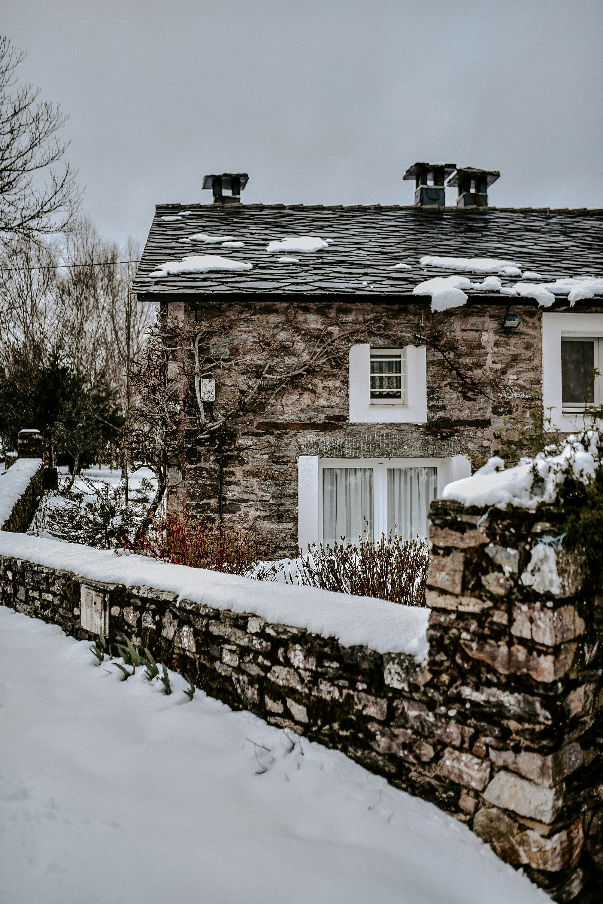 A stone house covered in snow next to a stone fence