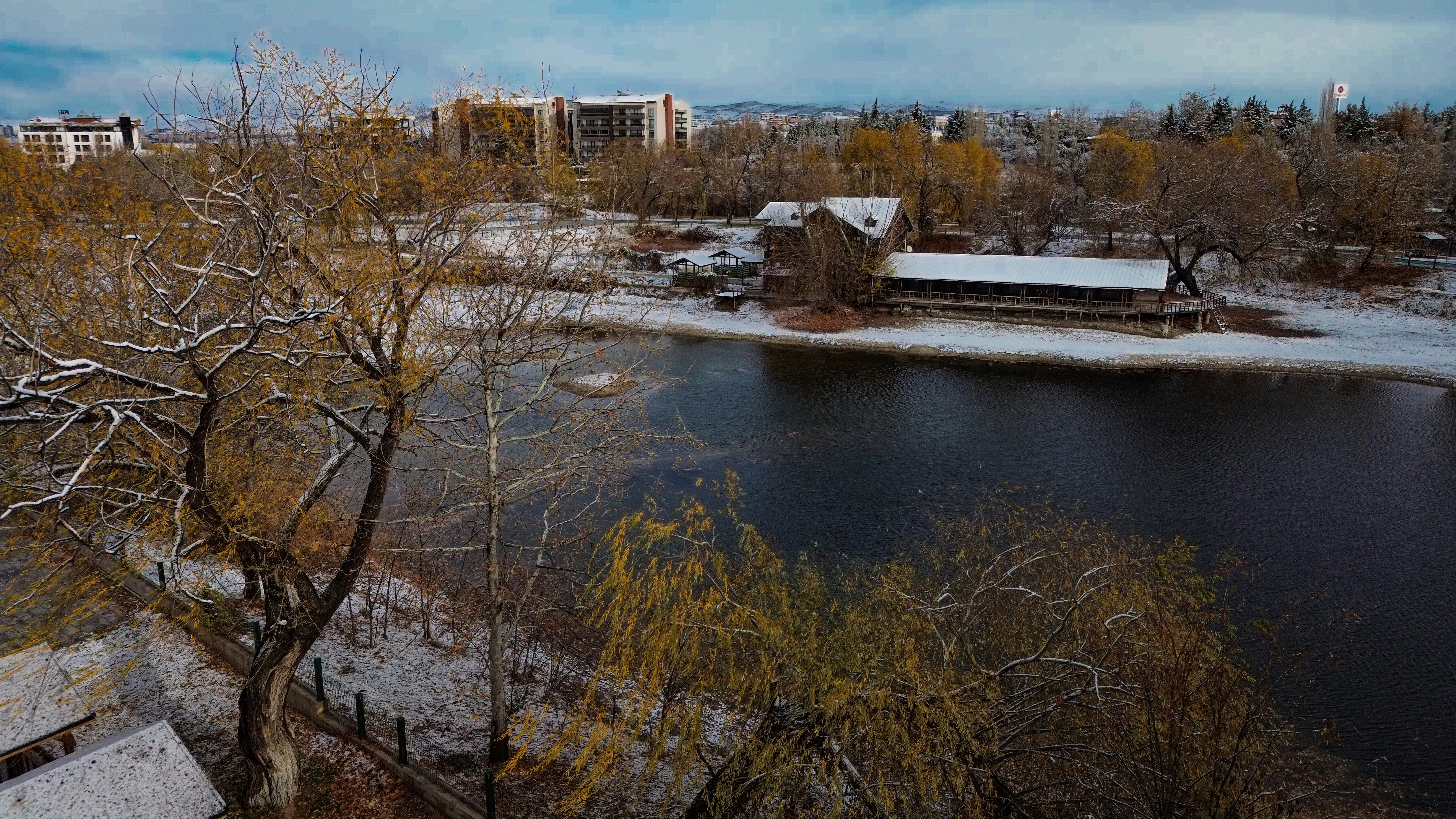 A lake surrounded by trees and buildings under a cloudy sky
