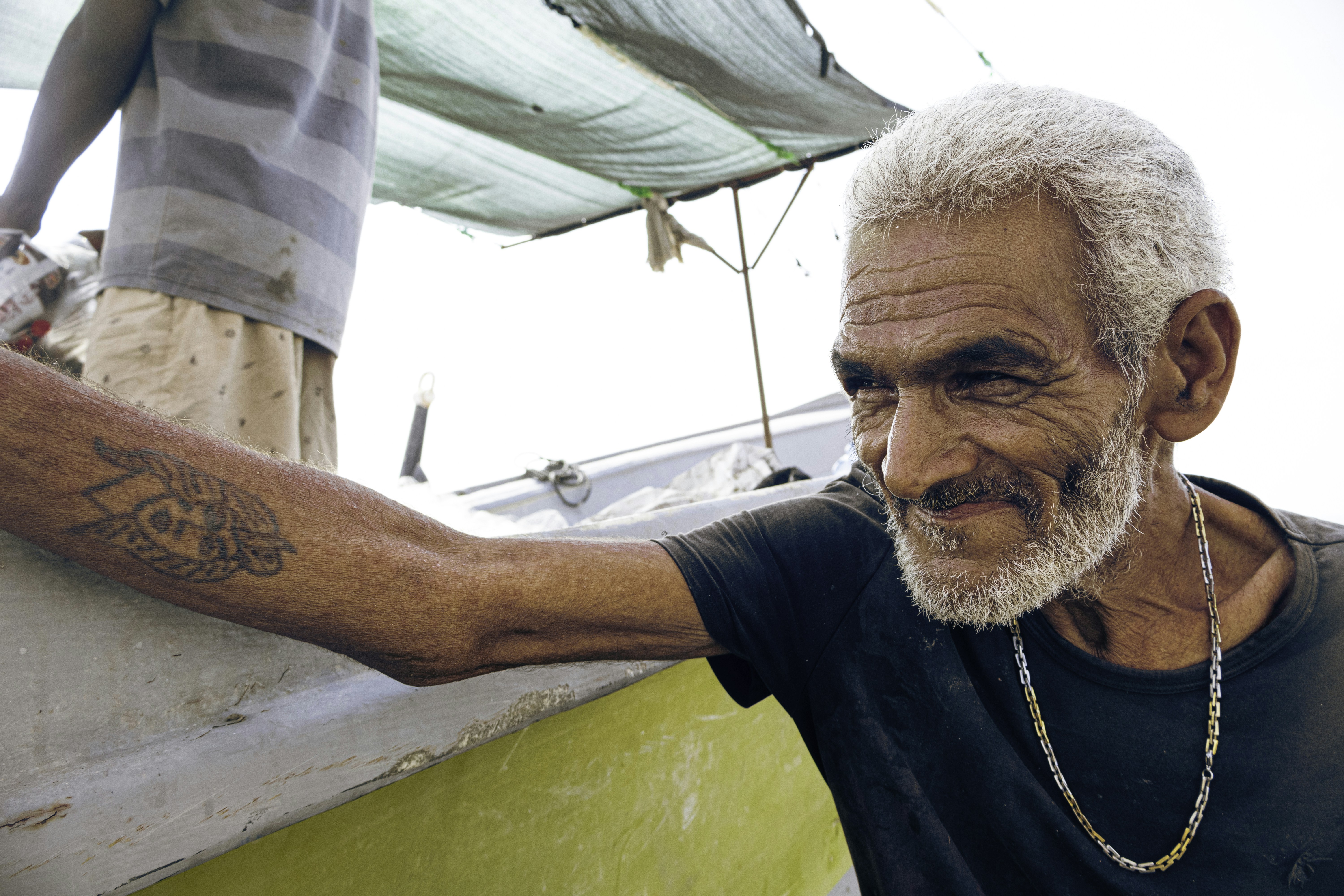 A man with a beard and tattoos on his arm leaning on a boat