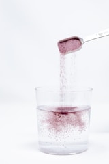 A spoon pouring red liquid into a glass