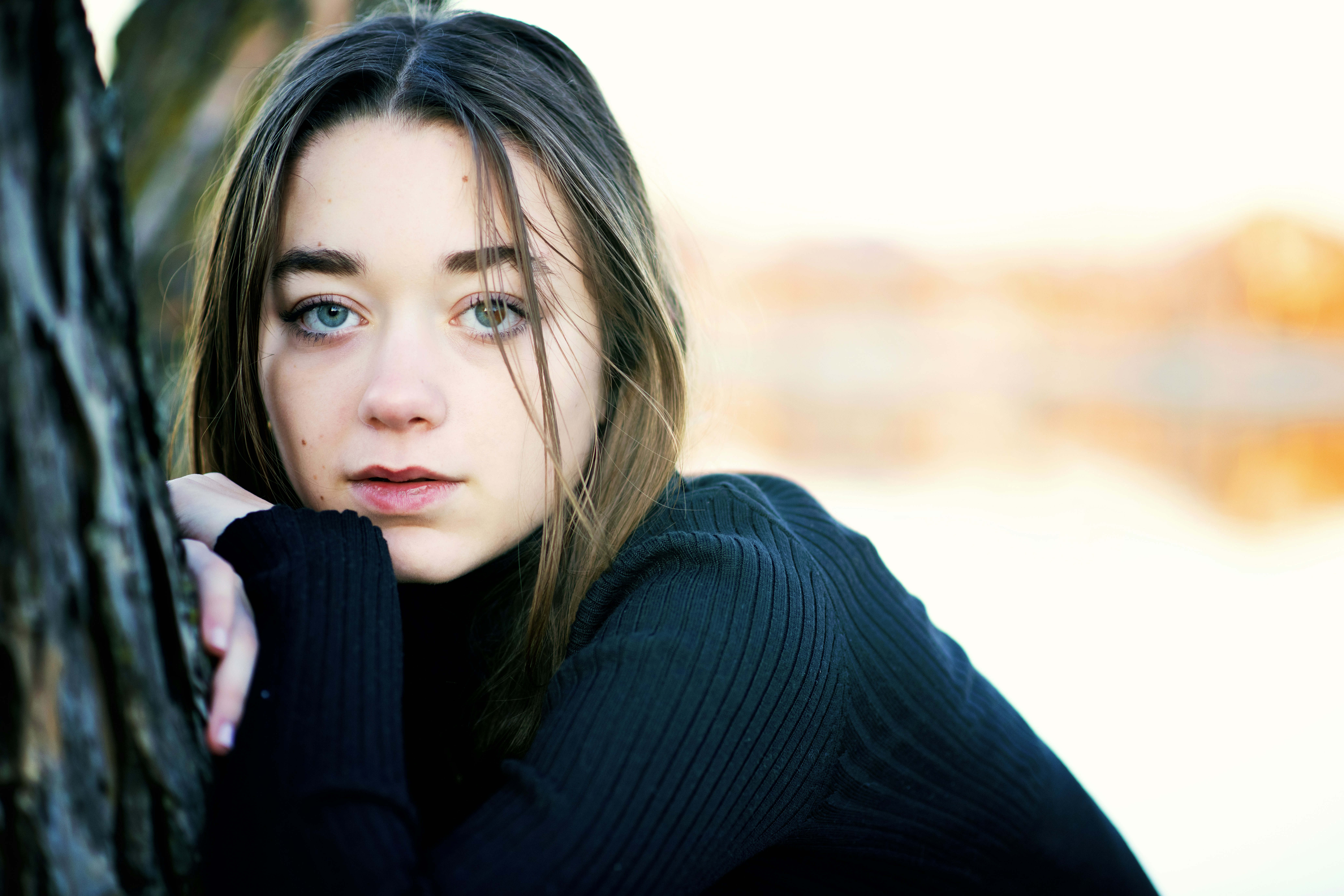 A woman leaning against a tree with her hand on her shoulder